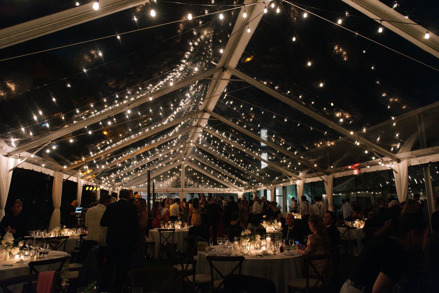Clear tent reception venue illuminated with romantic string lights creating a magical evening atmosphere.