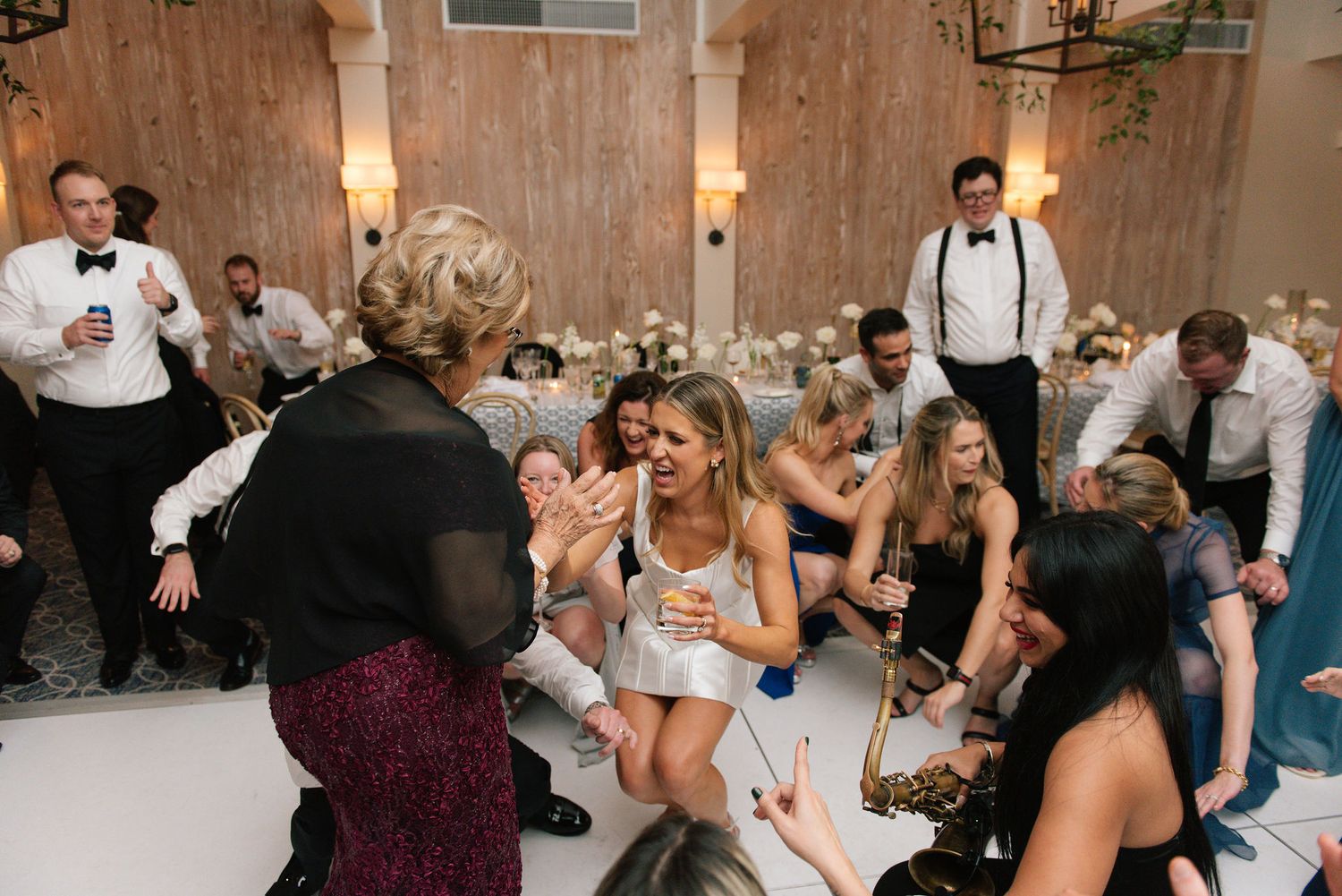 Wedding guests dancing and celebrating on a rustic venue dance floor with wooden walls and warm lighting.