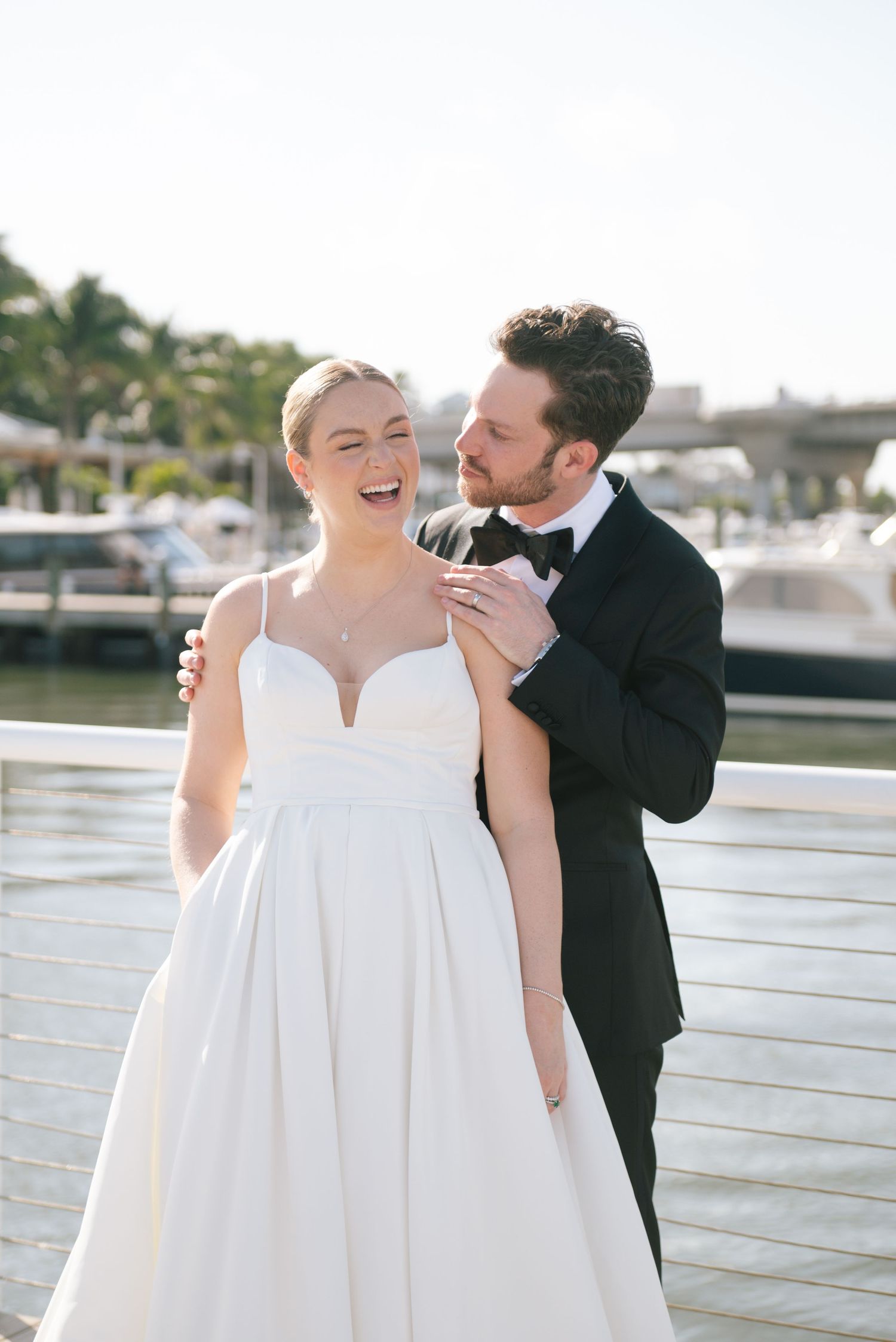 A romantic moment captured on a sunny waterfront deck during a wedding celebration.