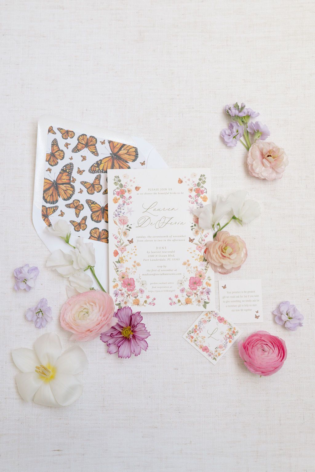 Wedding stationery with butterfly motifs and floral designs laid out with fresh pink and purple blooms.
