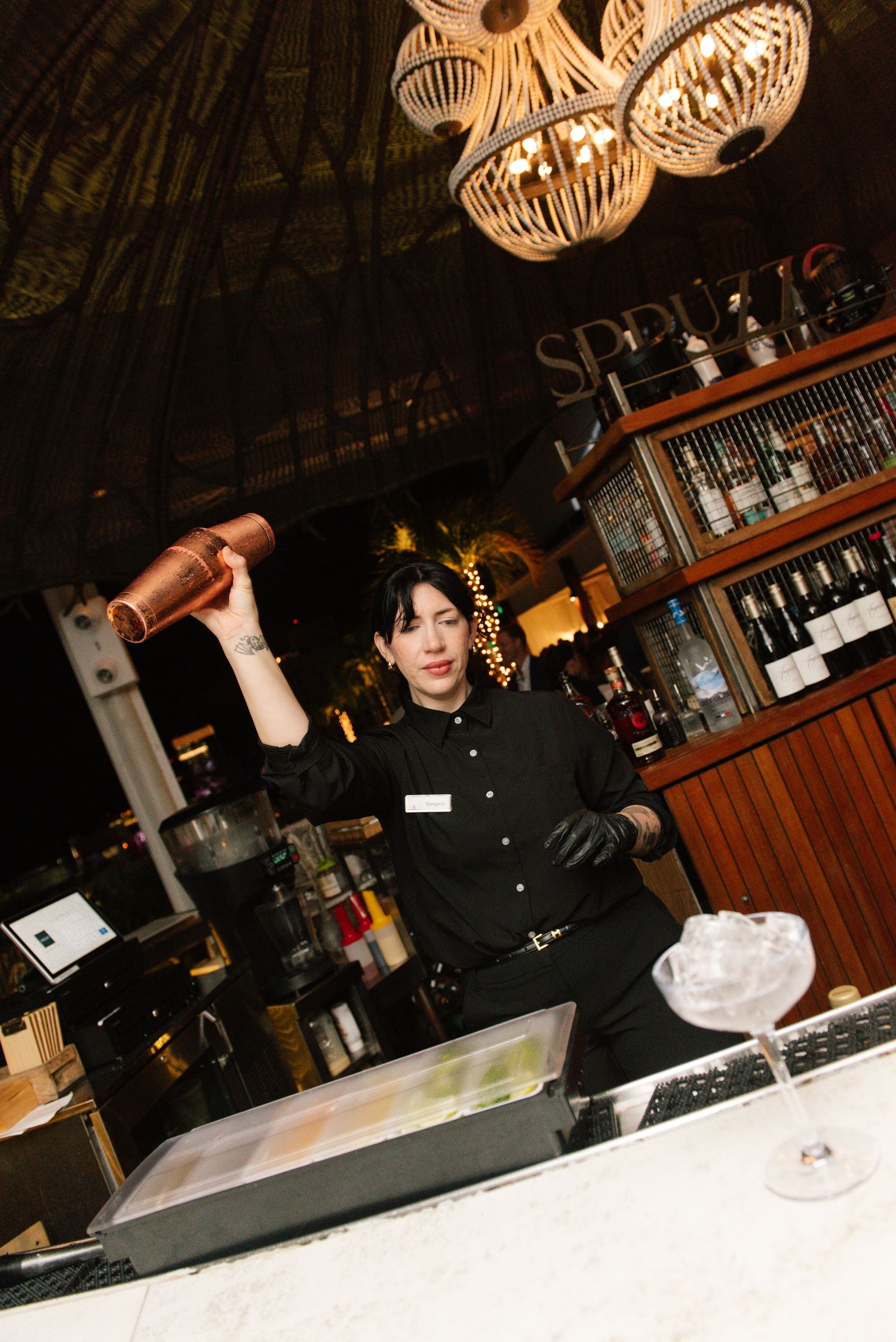 Bartender mixing drinks under decorative pendant lights at an elegant bar.