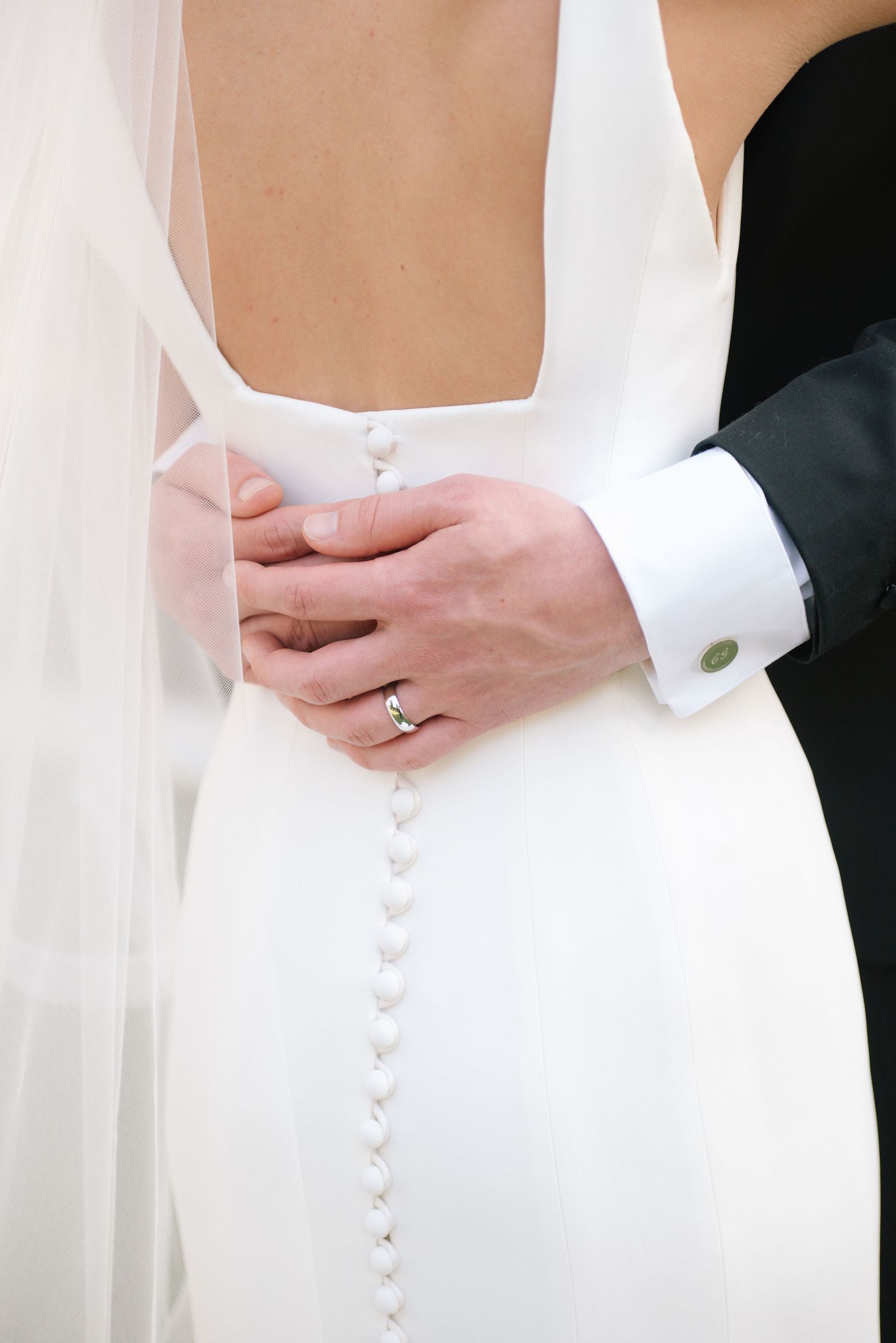 Close-up detail of elegant white wedding dress buttons and flowing veil.