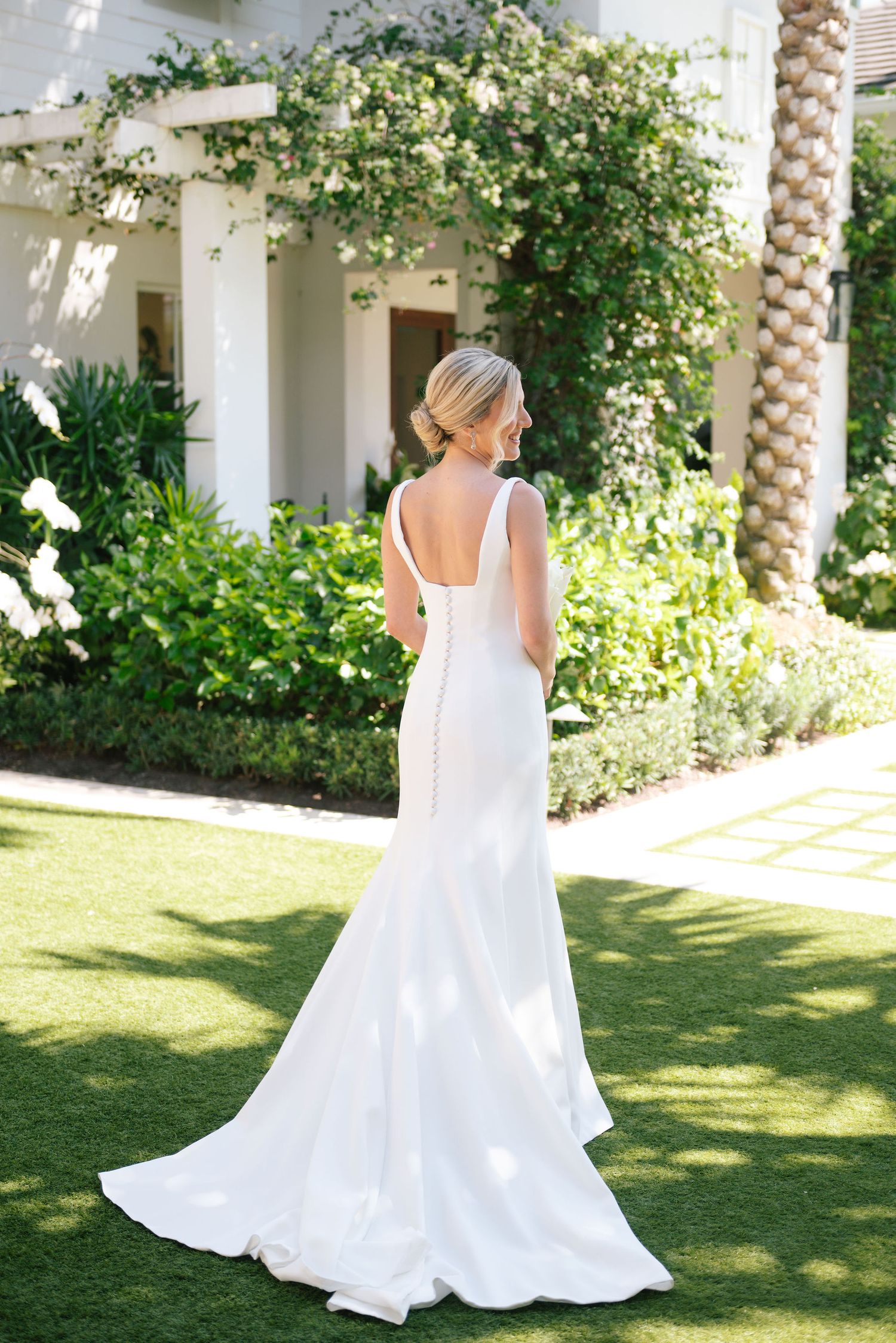 Back view of flowing white wedding gown against lush garden backdrop.