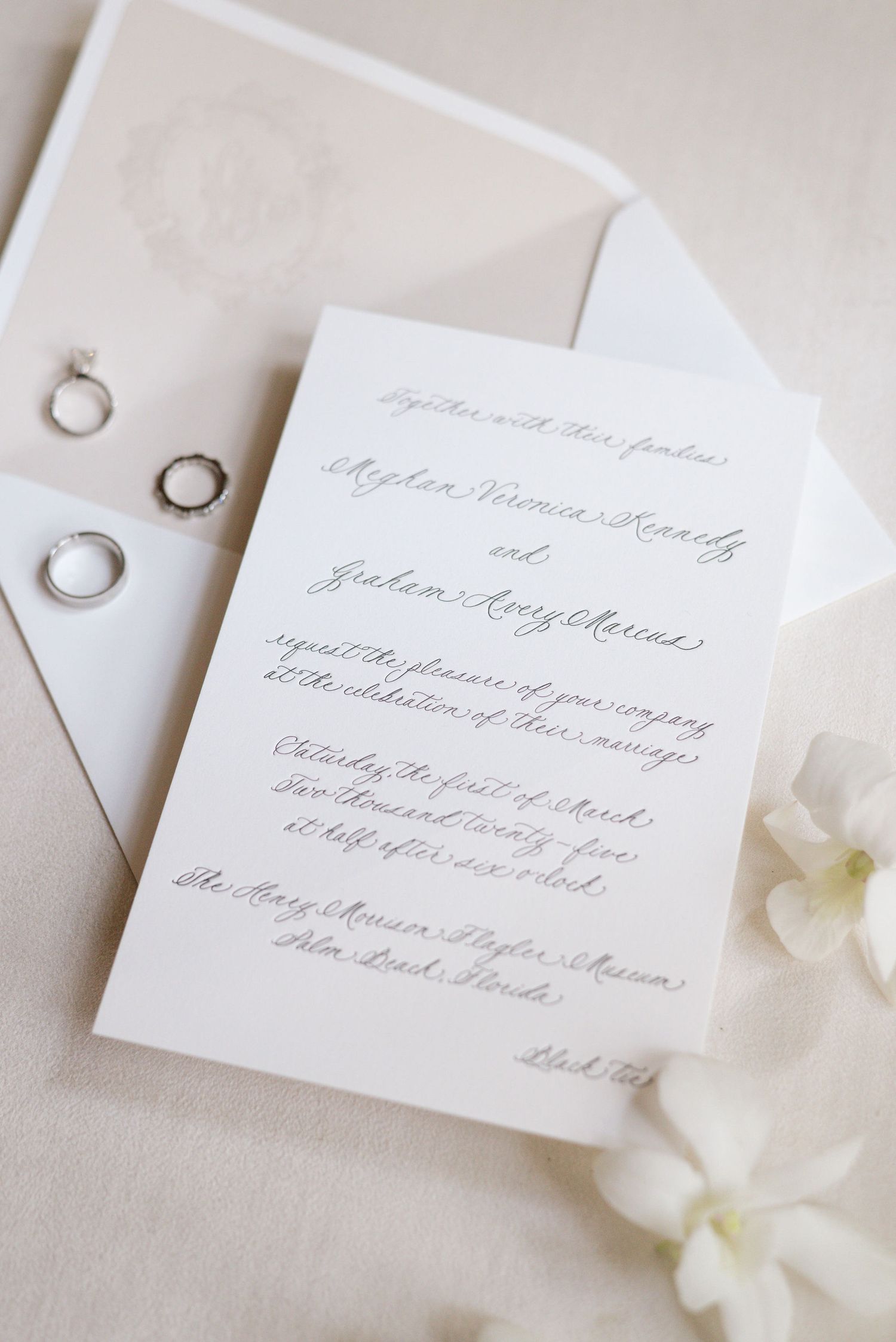 Elegant wedding invitation with delicate calligraphy and wedding rings on white linen.