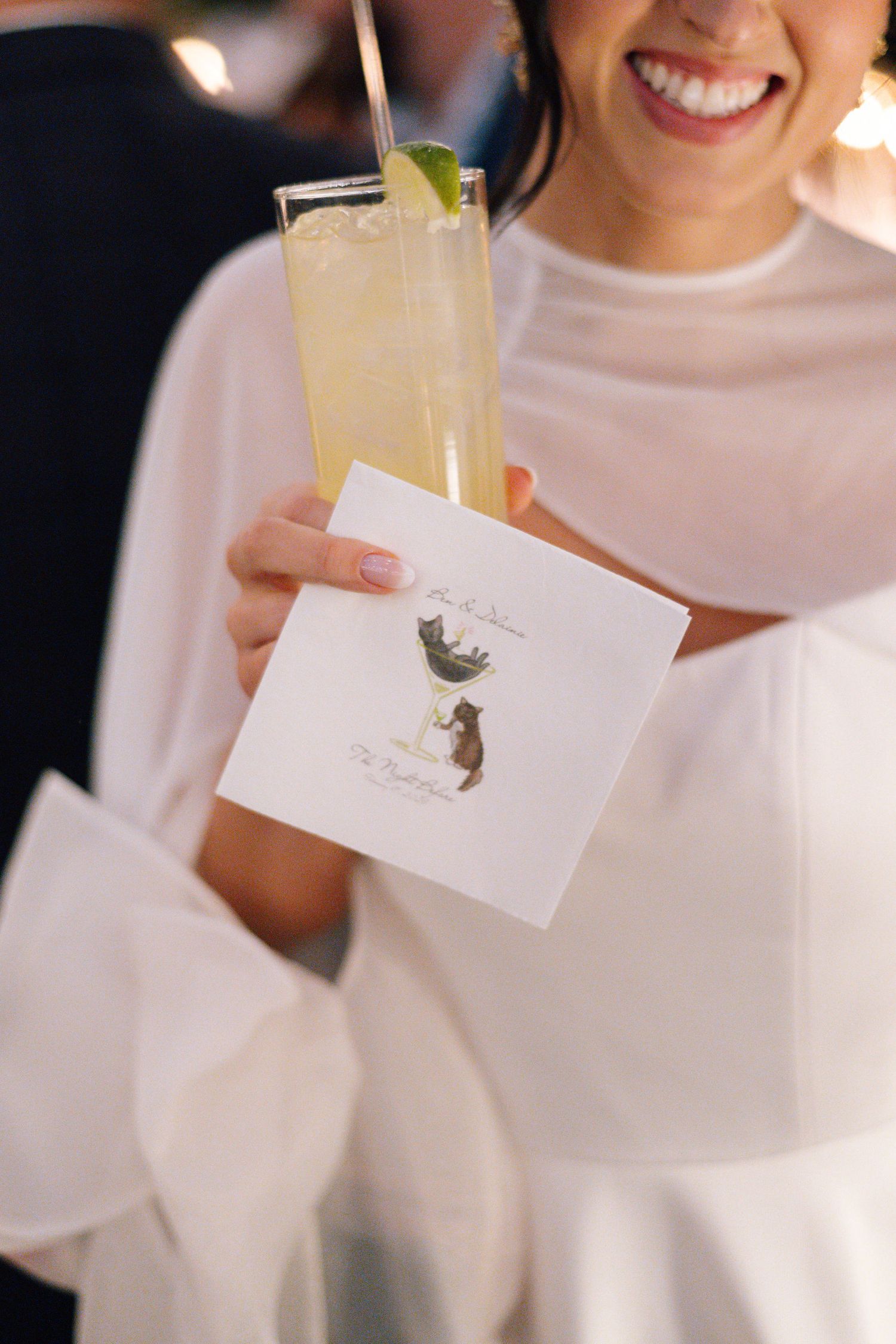 A hand holds a refreshing cocktail and wedding favor card with delicate artwork.