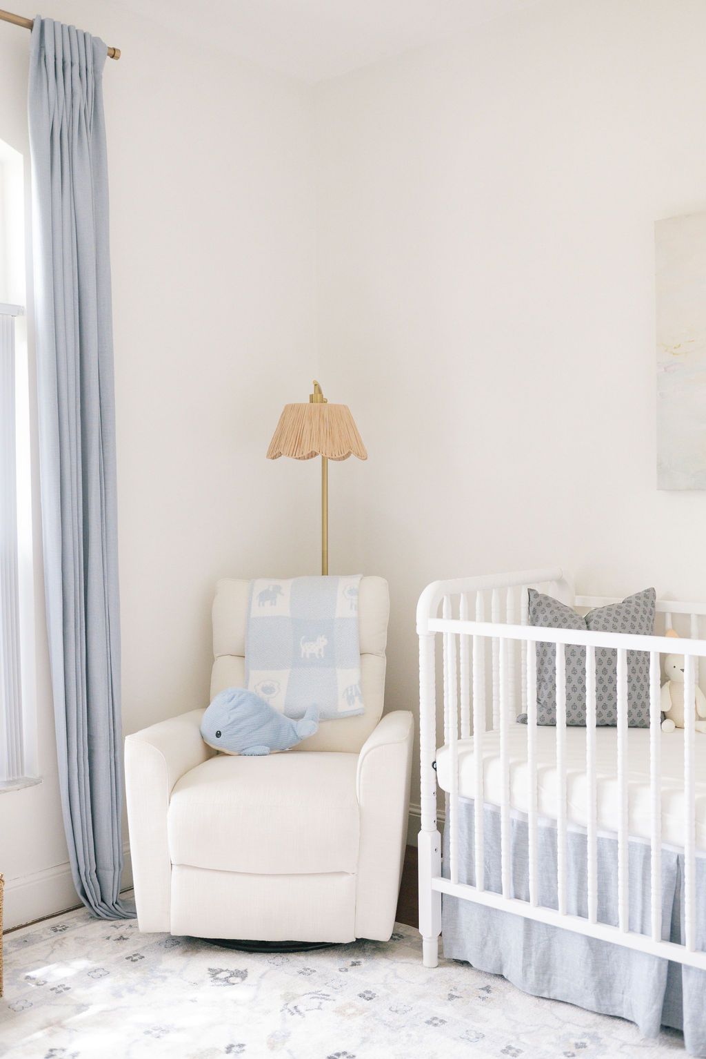 Serene nursery with white crib, blue curtains, and comfortable armchair in neutral tones.