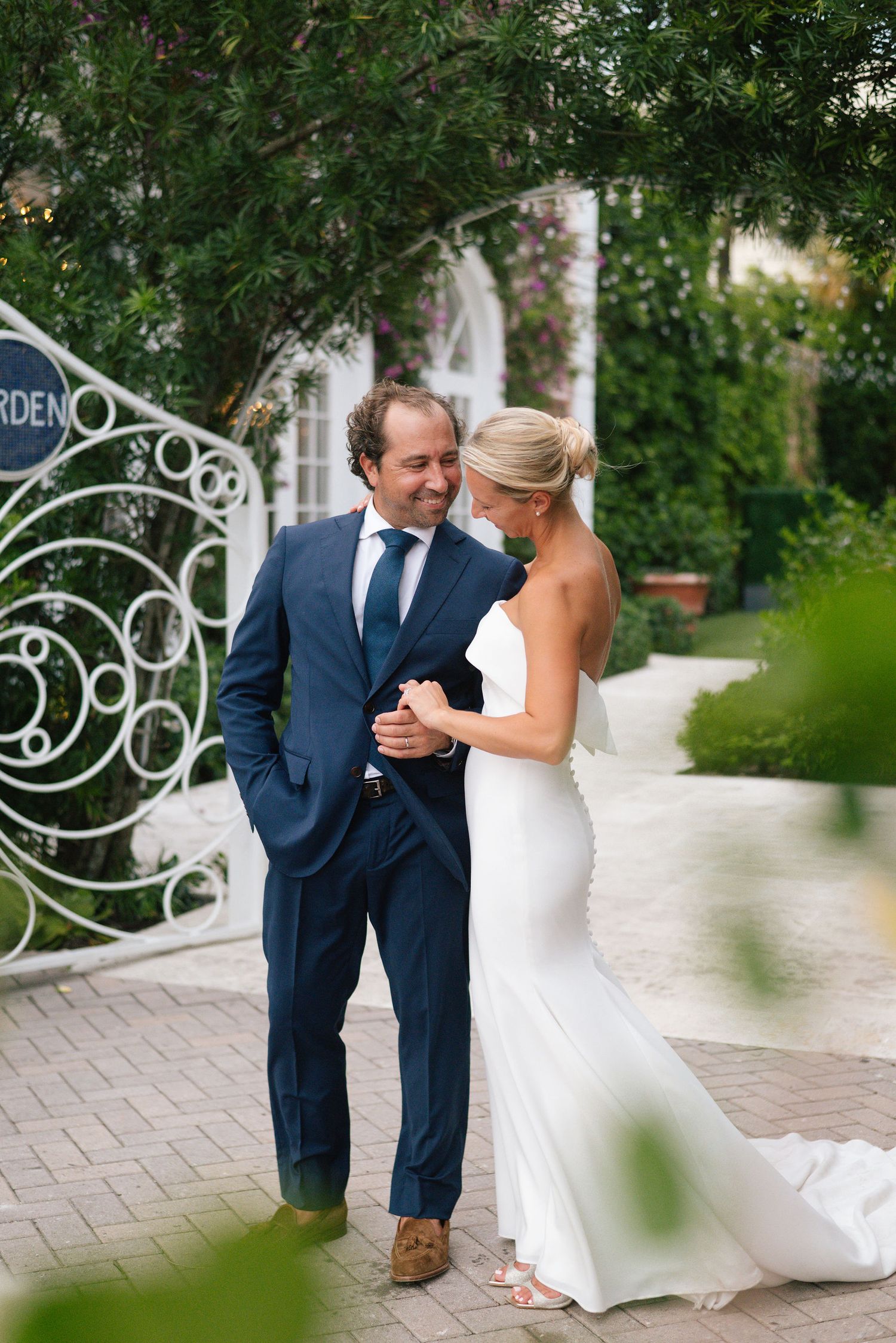 Romantic wedding portraits captured near ornate garden gate with tropical foliage.