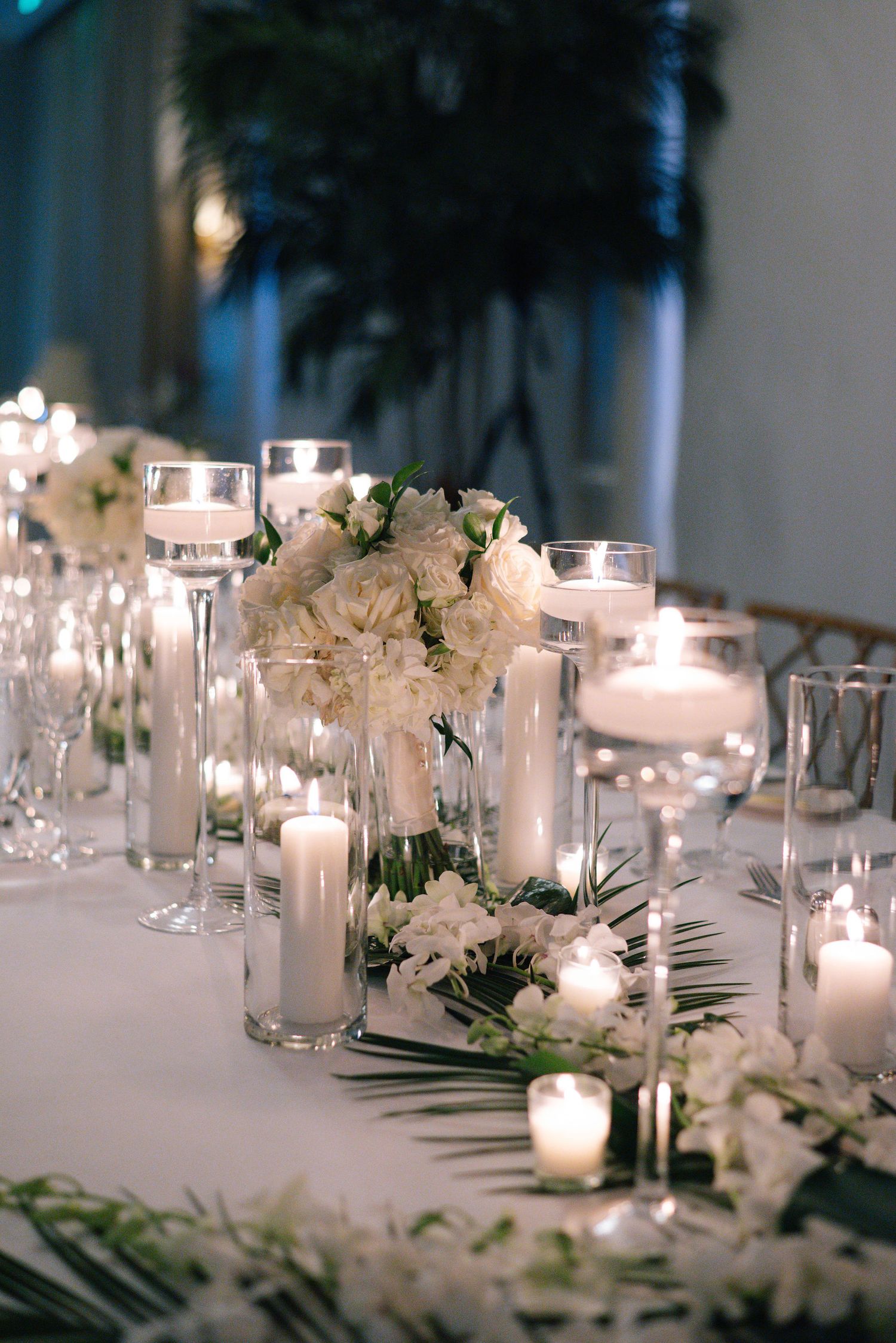 Romantic table setting with white flowers and glowing candles in glass holders.