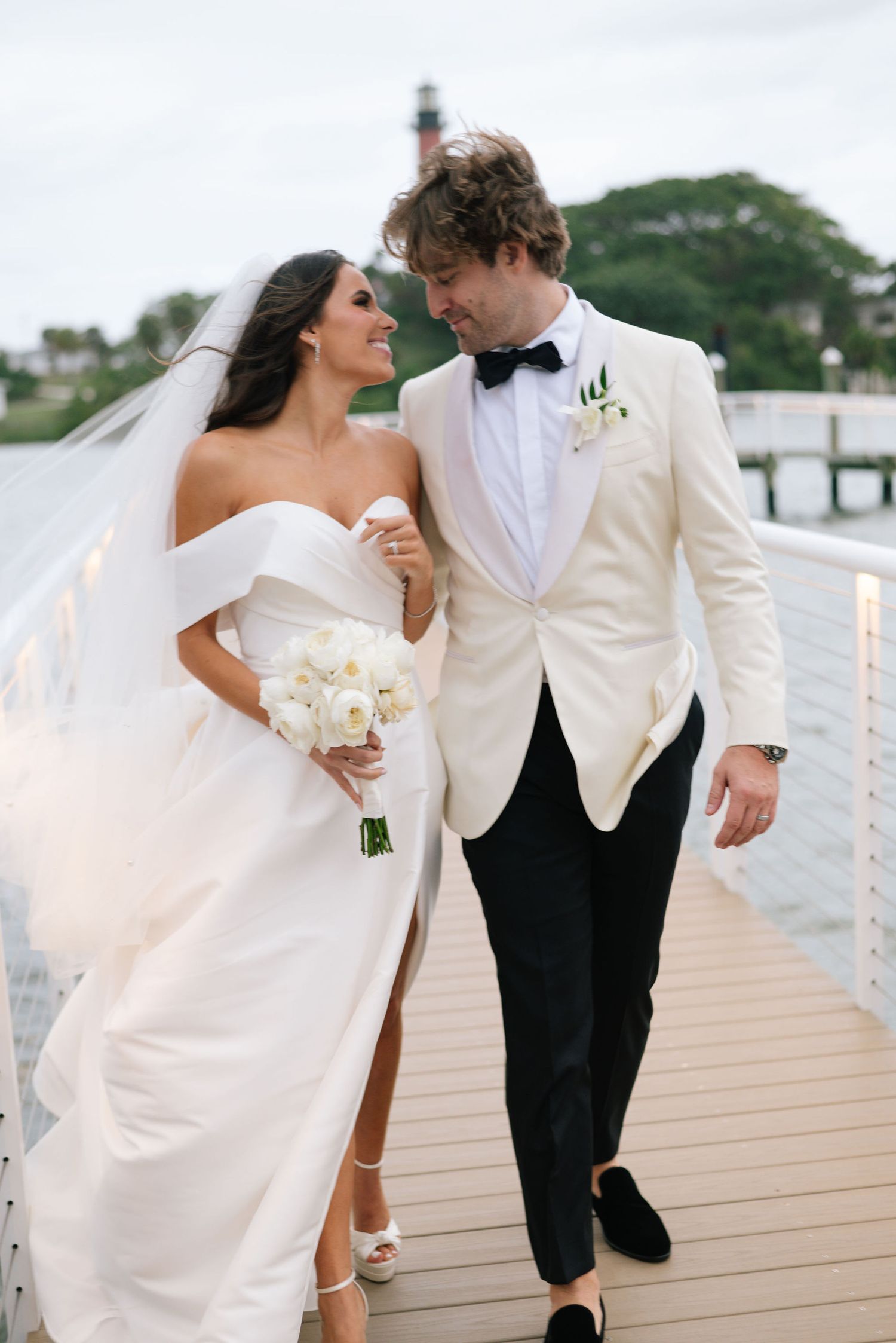 Newlyweds share candid moments walking along waterfront boardwalk.