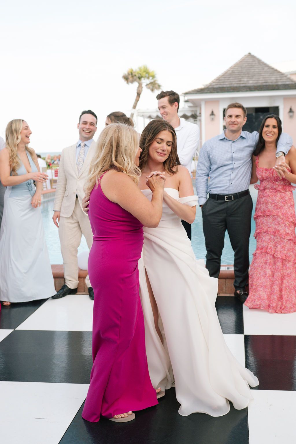 Wedding celebration with guests dancing on a checkerboard floor near a swimming pool at dusk.