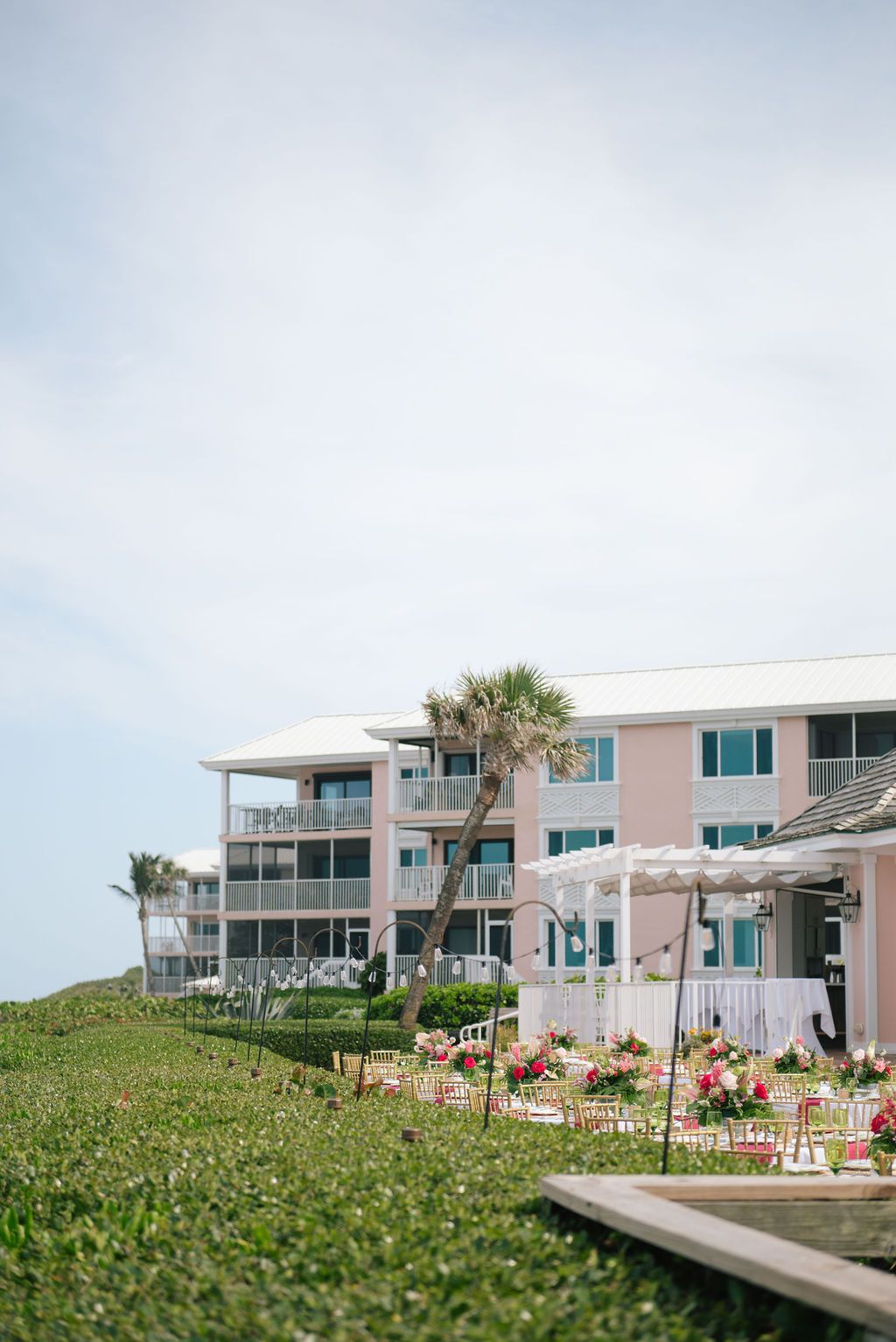 Beachfront venue with modern white buildings and palm trees set against a cloudy sky.