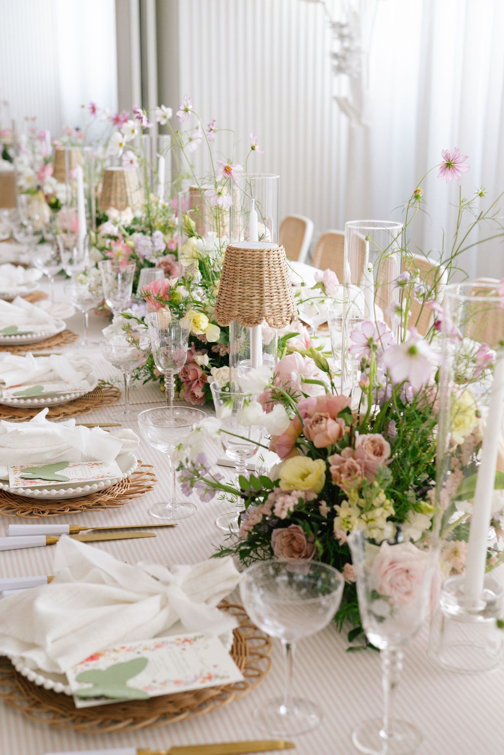 Elegant table setting with woven chargers, crystal glasses and pink floral arrangements.