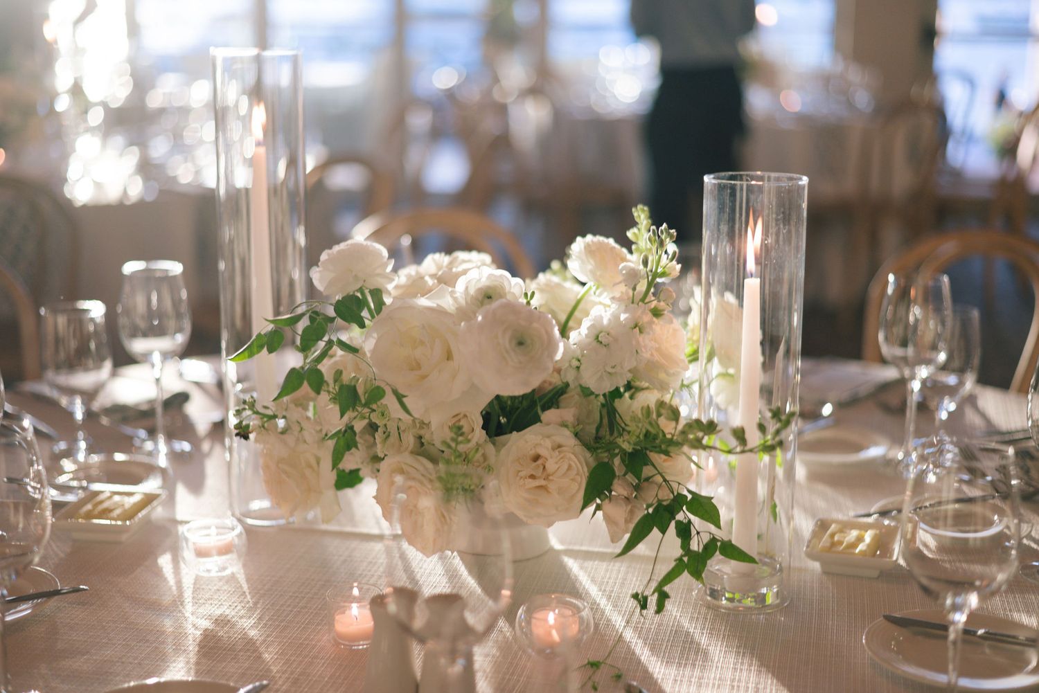 Elegant wedding reception tables set with white linens, glassware and floral centerpieces in a banquet hall.