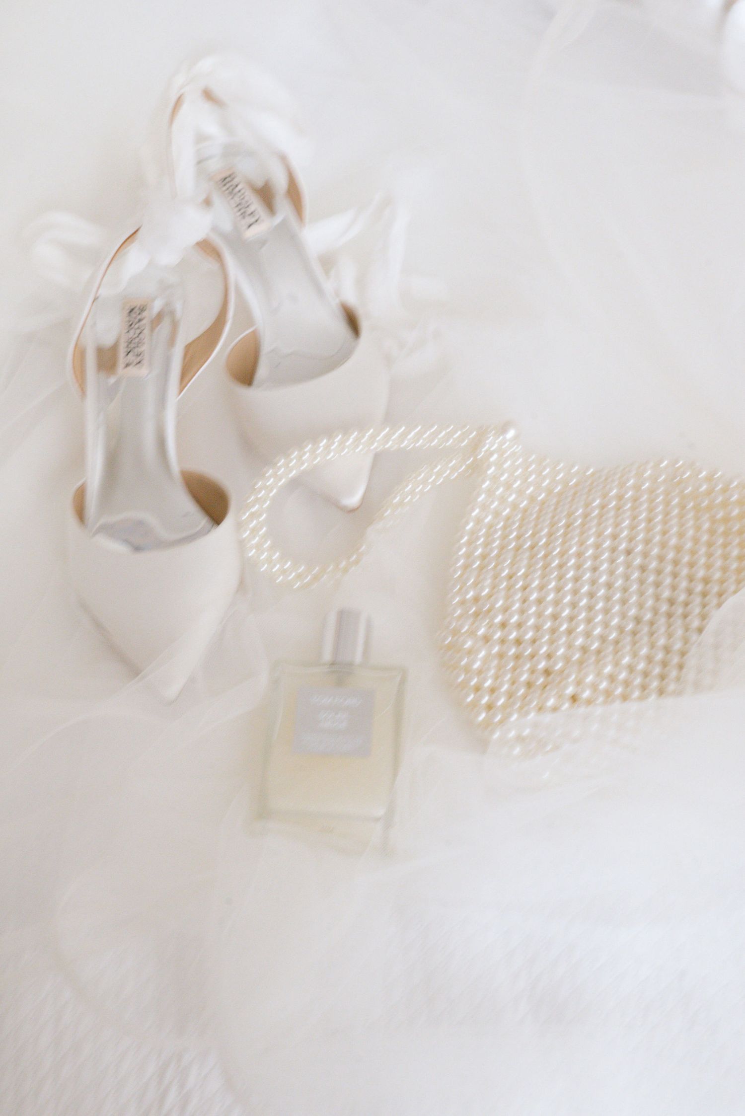 Elegant white perfume bottle and pearl necklace arranged on soft white fabric in a minimalist style.