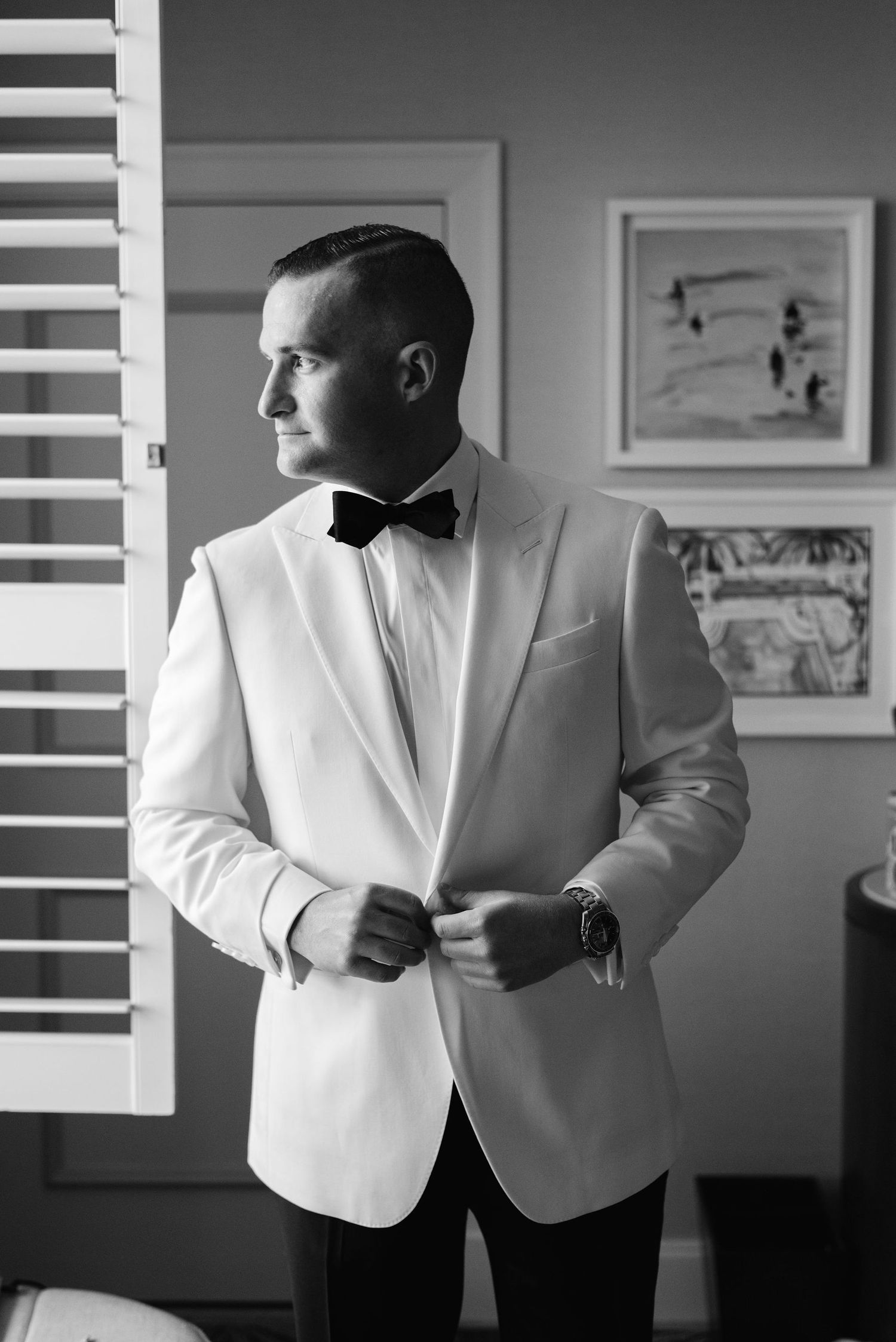 Black and white photos of groom adjusting white tuxedo jacket before wedding ceremony.