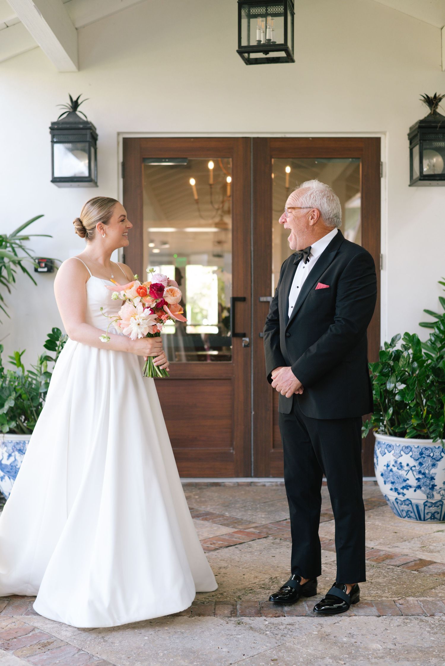 Emotional first look between a bride in white gown and older man in tuxedo on a covered porch.