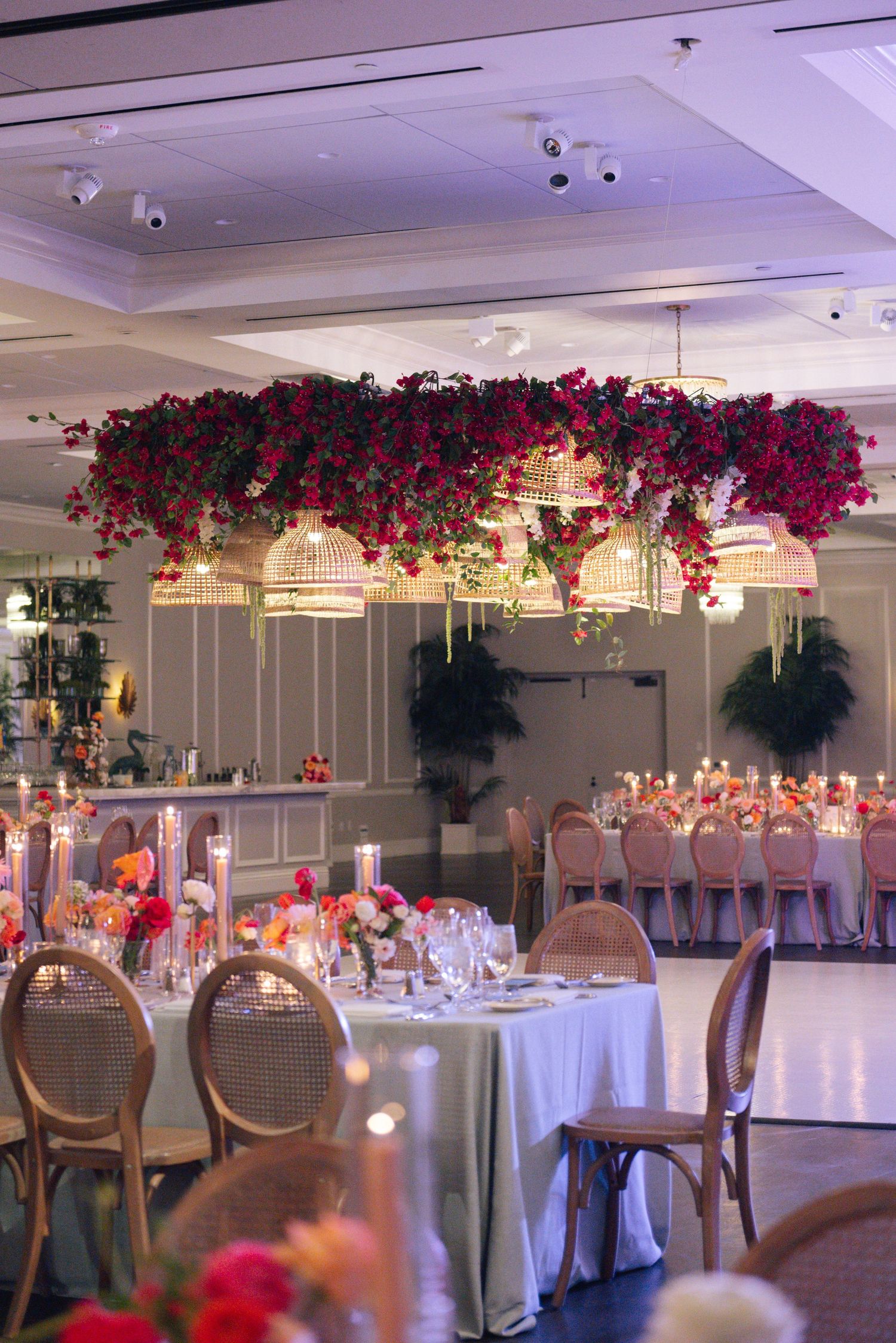 Wedding reception venue with dramatic pink floral ceiling installation and white table settings.