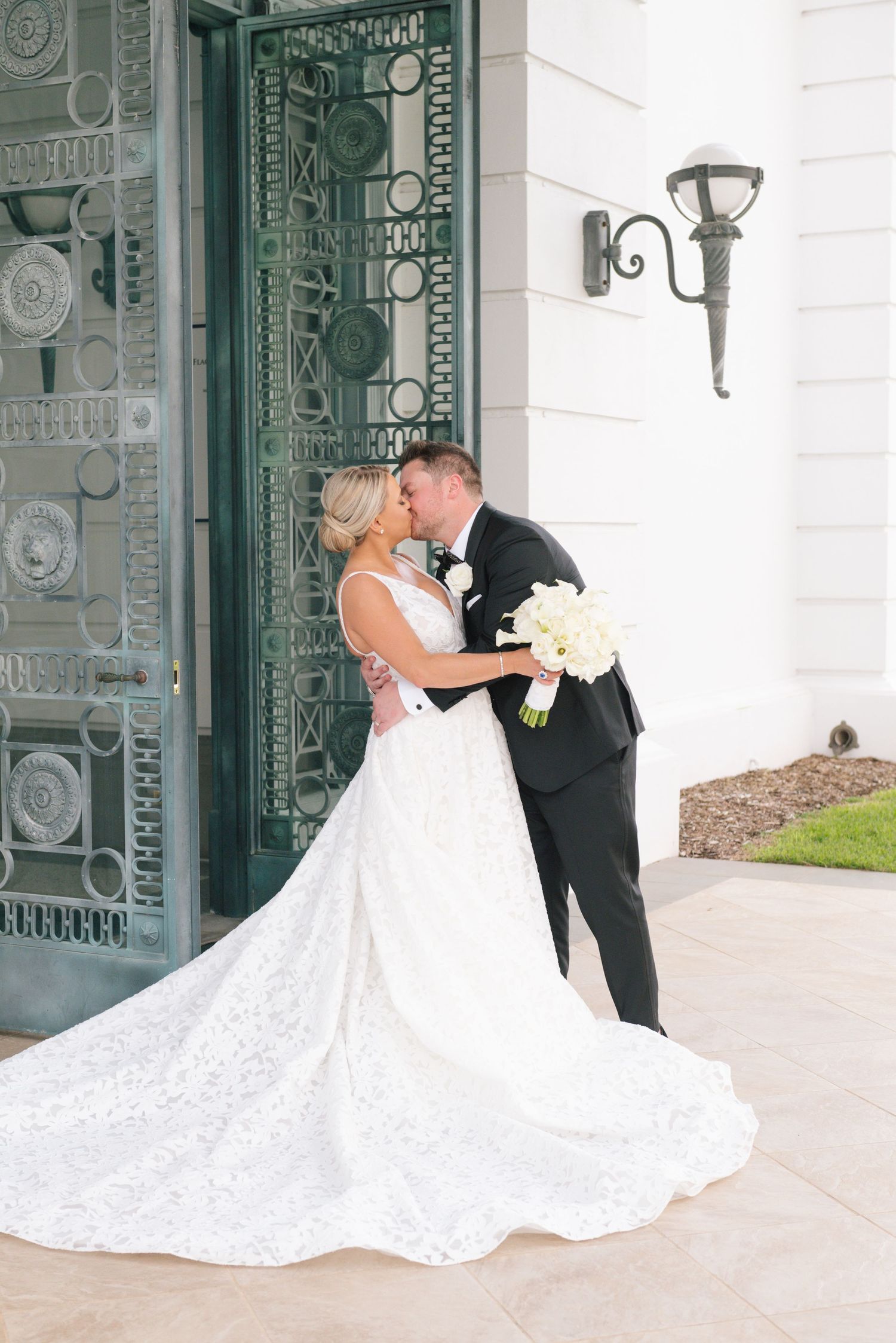 Bride and groom sharing first kiss in front of ornate green doors in wedding attire.