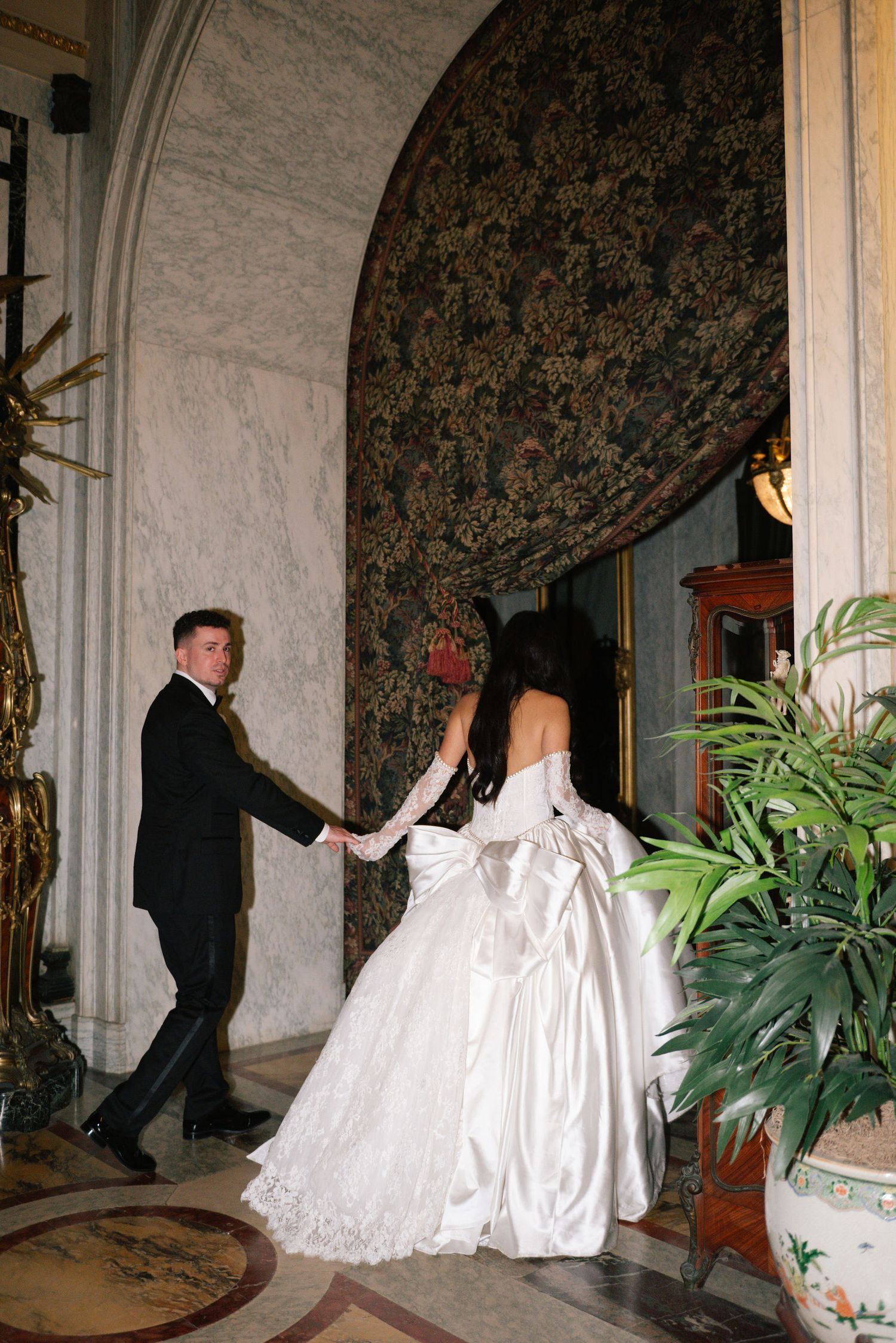 A couple navigates through an elegant hallway with marble walls and potted plants.