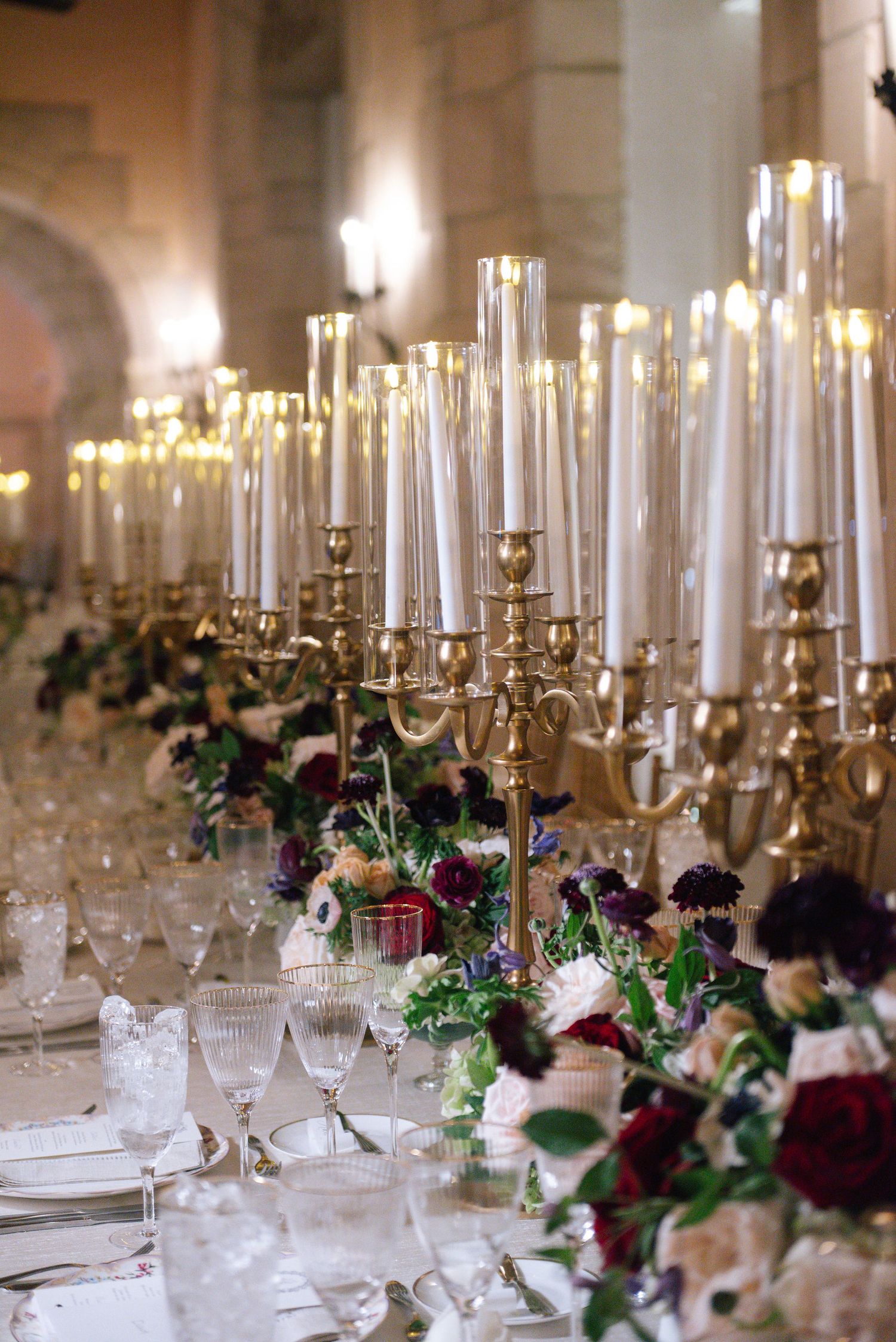 Crystal candleholders and deep red floral centerpieces line an elegant wedding reception table.