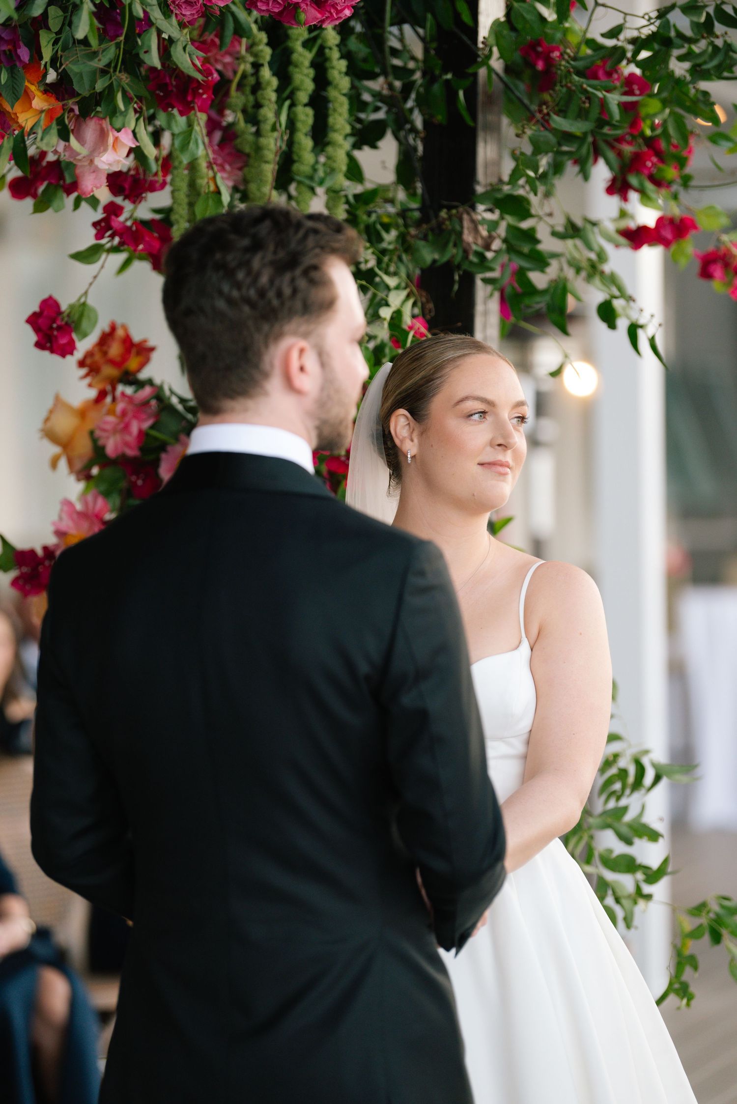 Wedding ceremony under floral arch with vibrant red and pink blooms.