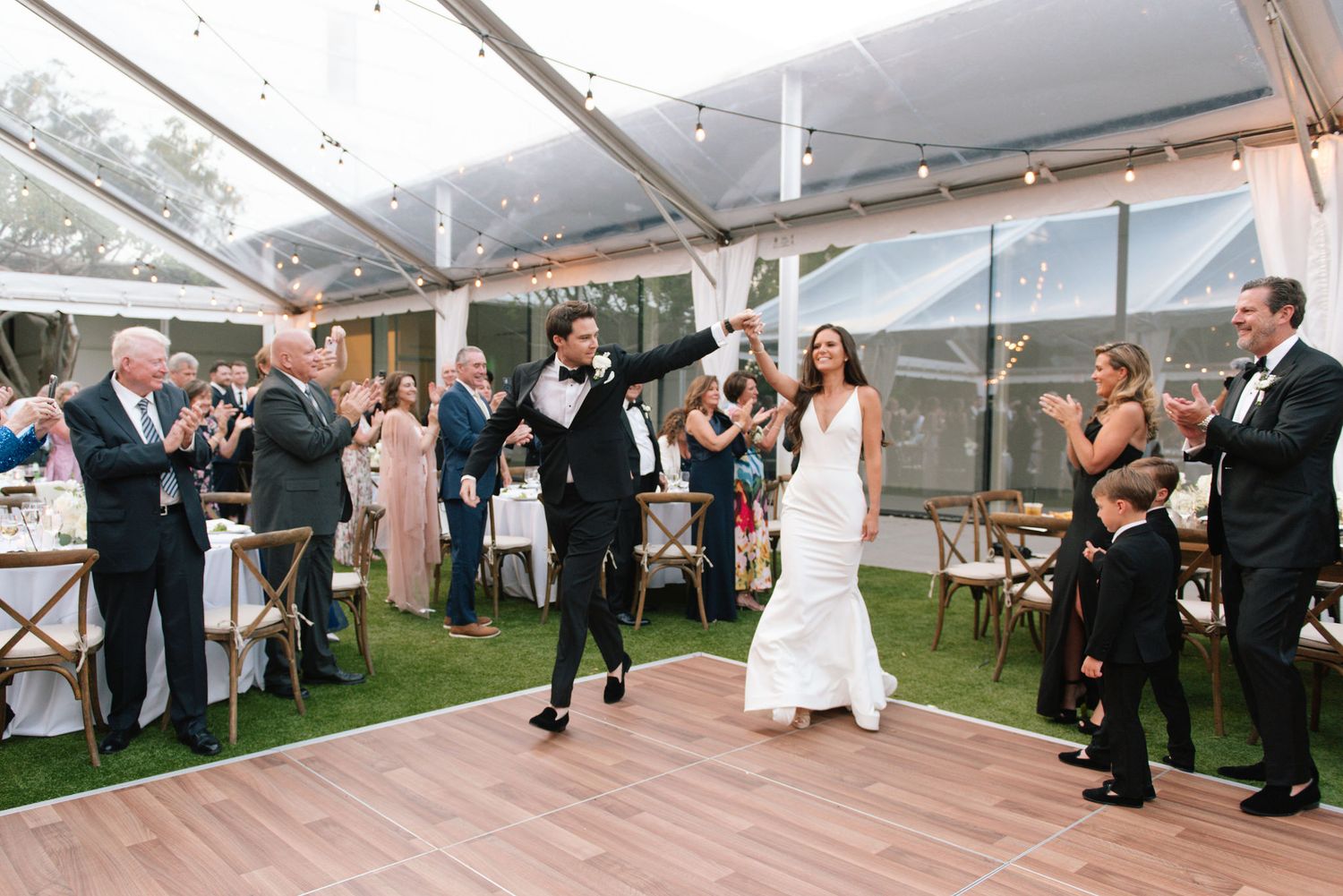 Wedding guests raise their glasses in celebration during an outdoor tent reception.