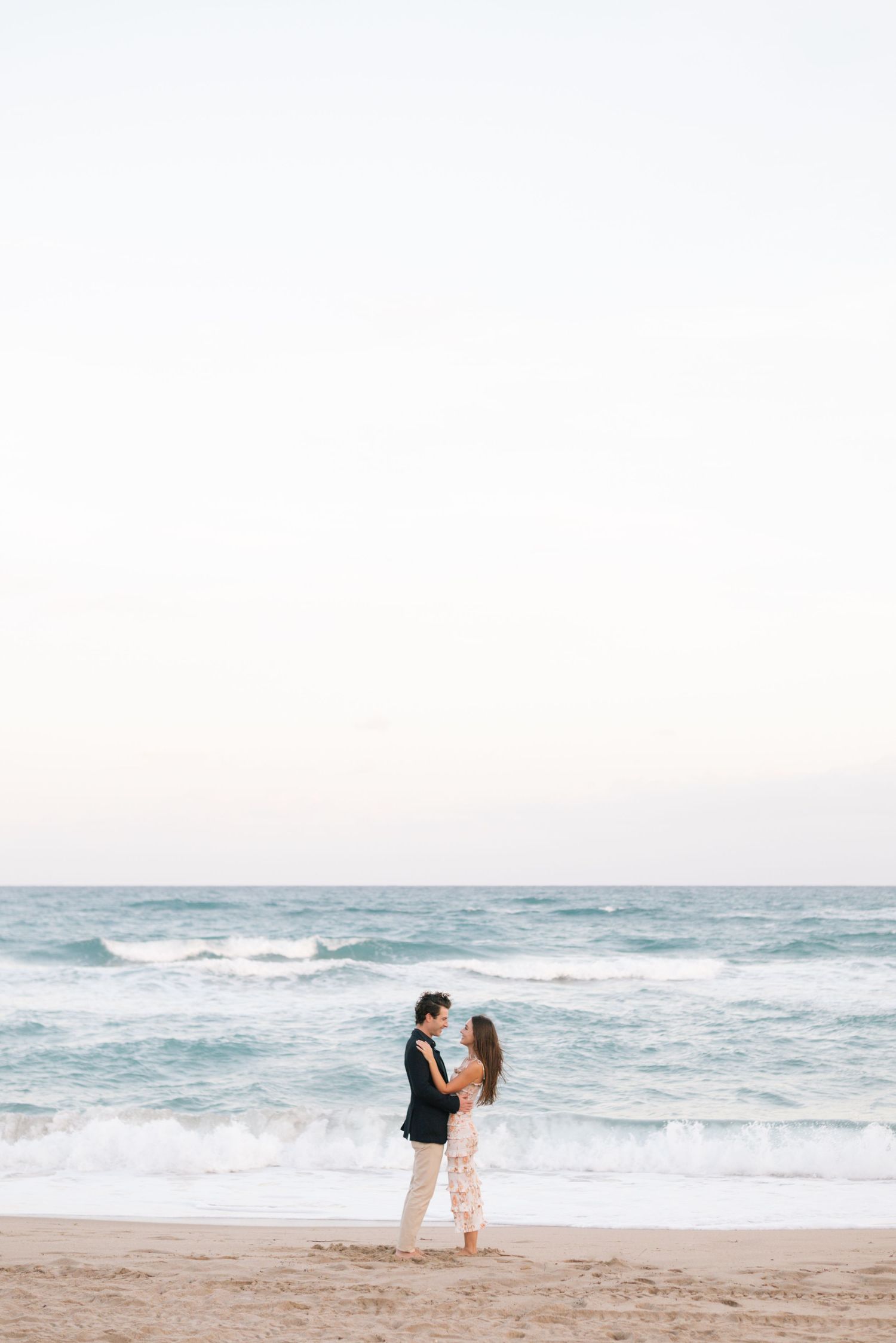 Couple walking hand in hand along a serene beach with crashing waves in the background.