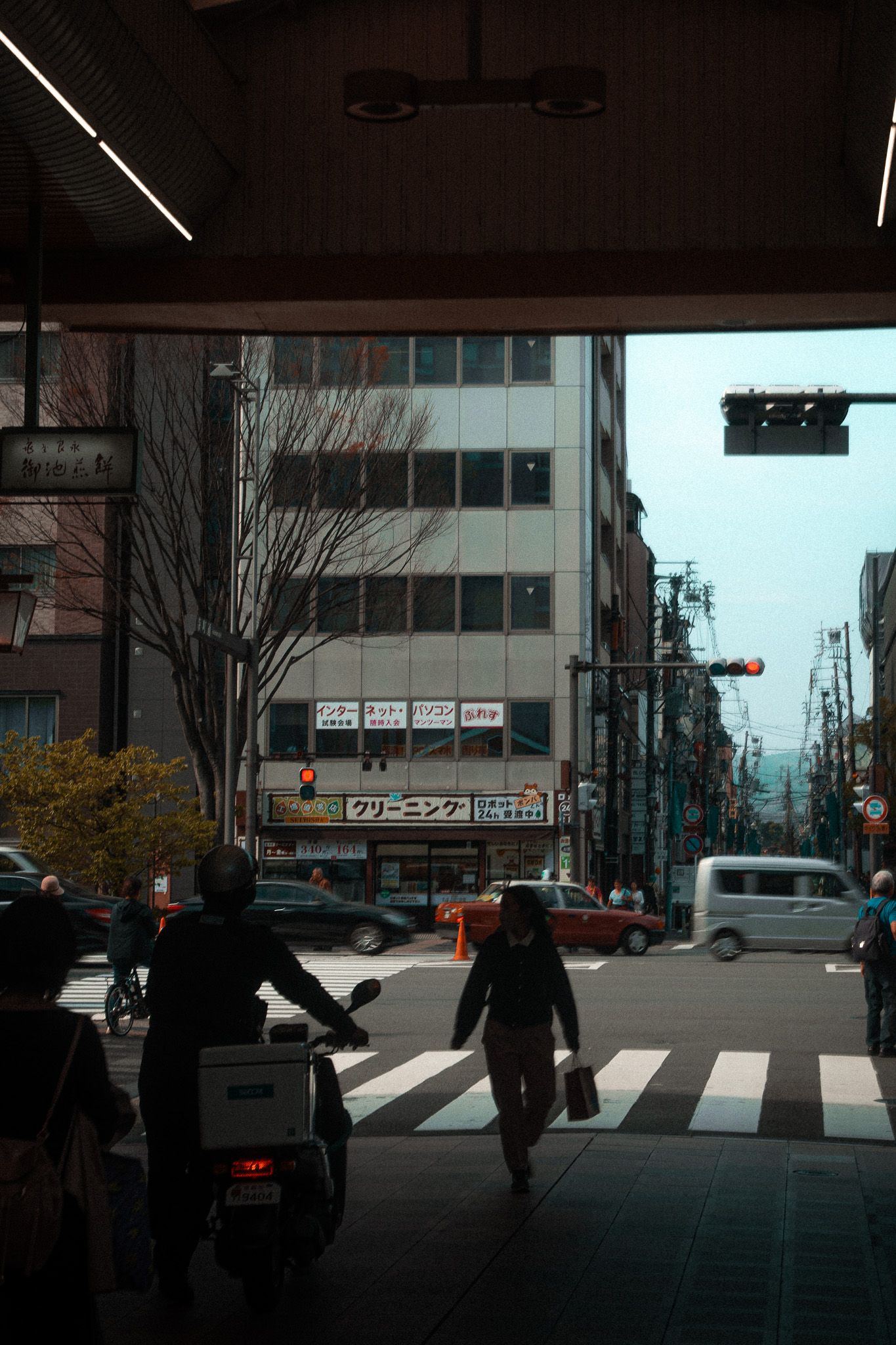 Urban street scene in Japan with pedestrians crossing under an overpass.