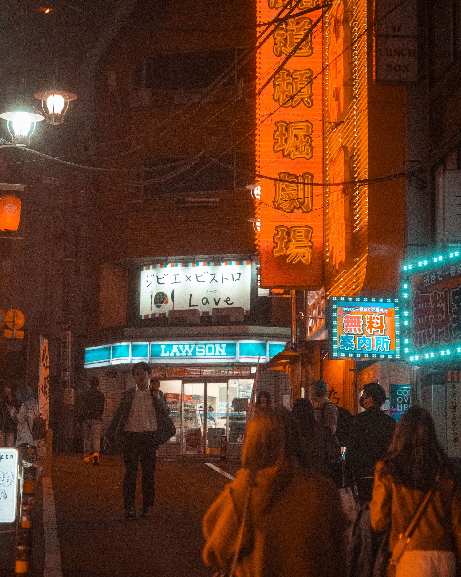 Nighttime street in Japan with glowing orange lanterns and neon signs.