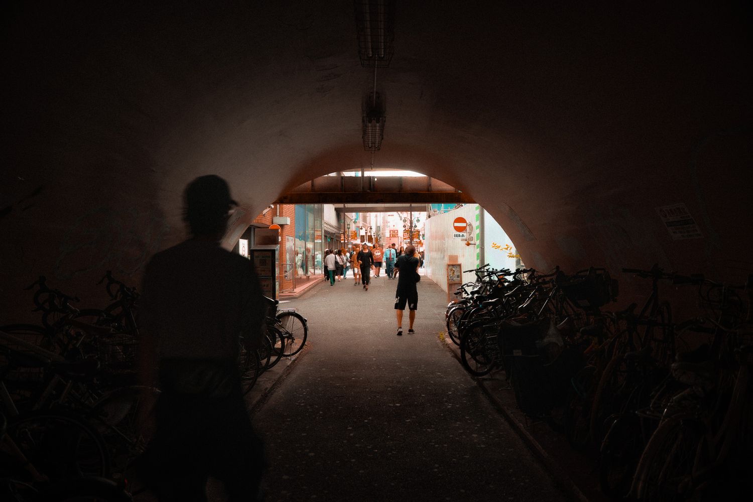 Dark tunnel with distant light and silhouetted figures creating atmospheric scene.