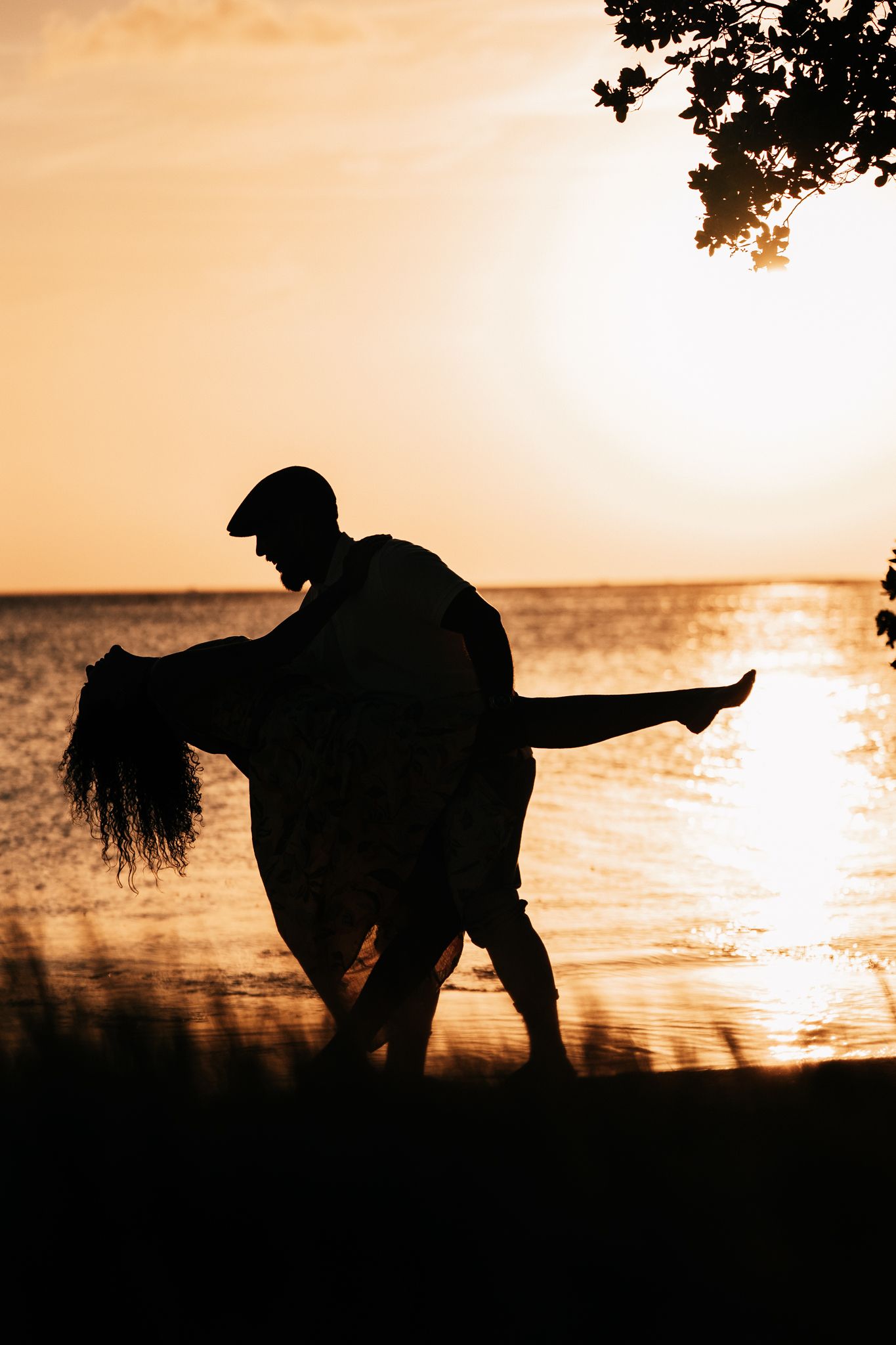 A silhouetted couple poses dramatically at sunset by the water.
