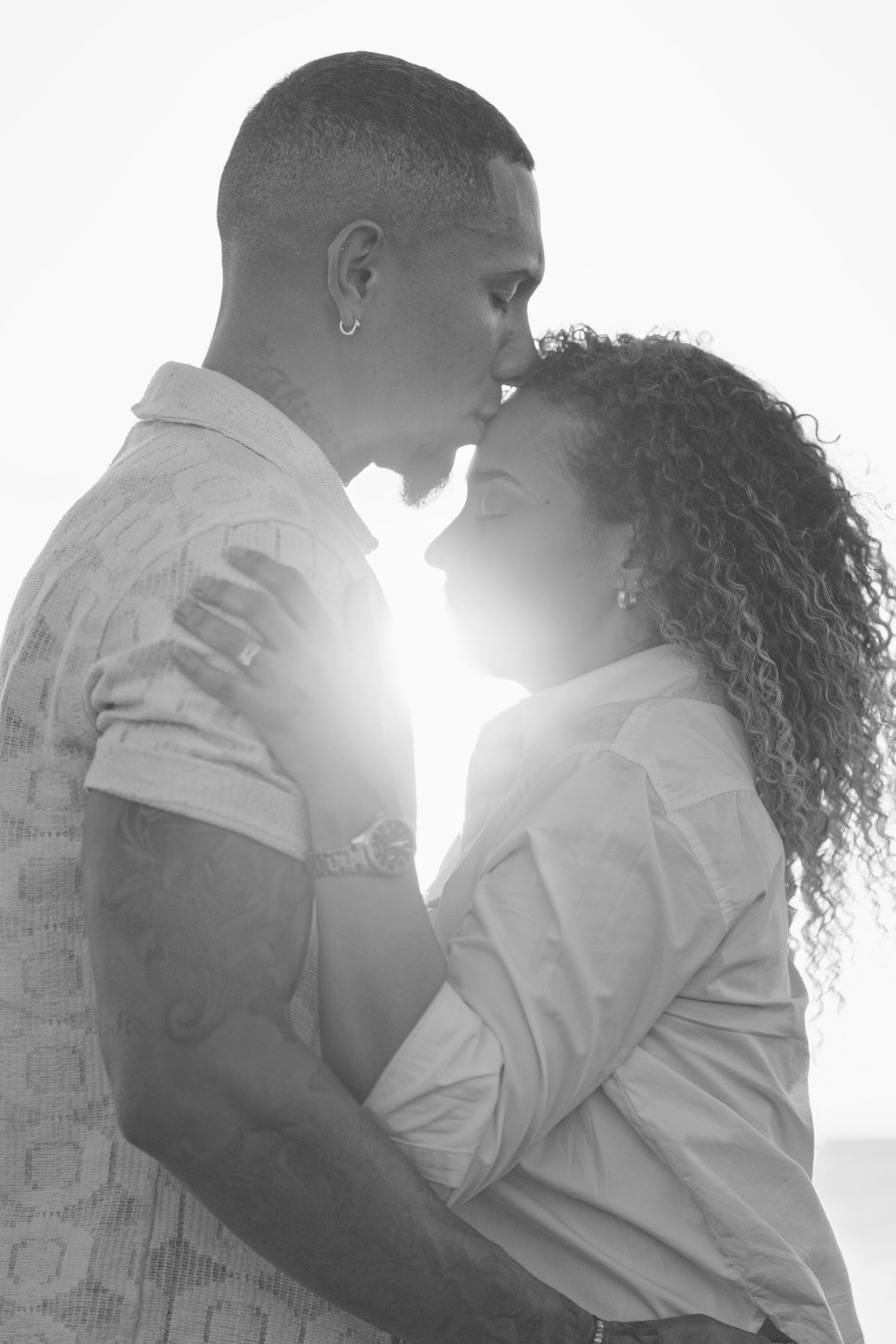 Backlit couple embracing in soft sunlight wearing white clothing.