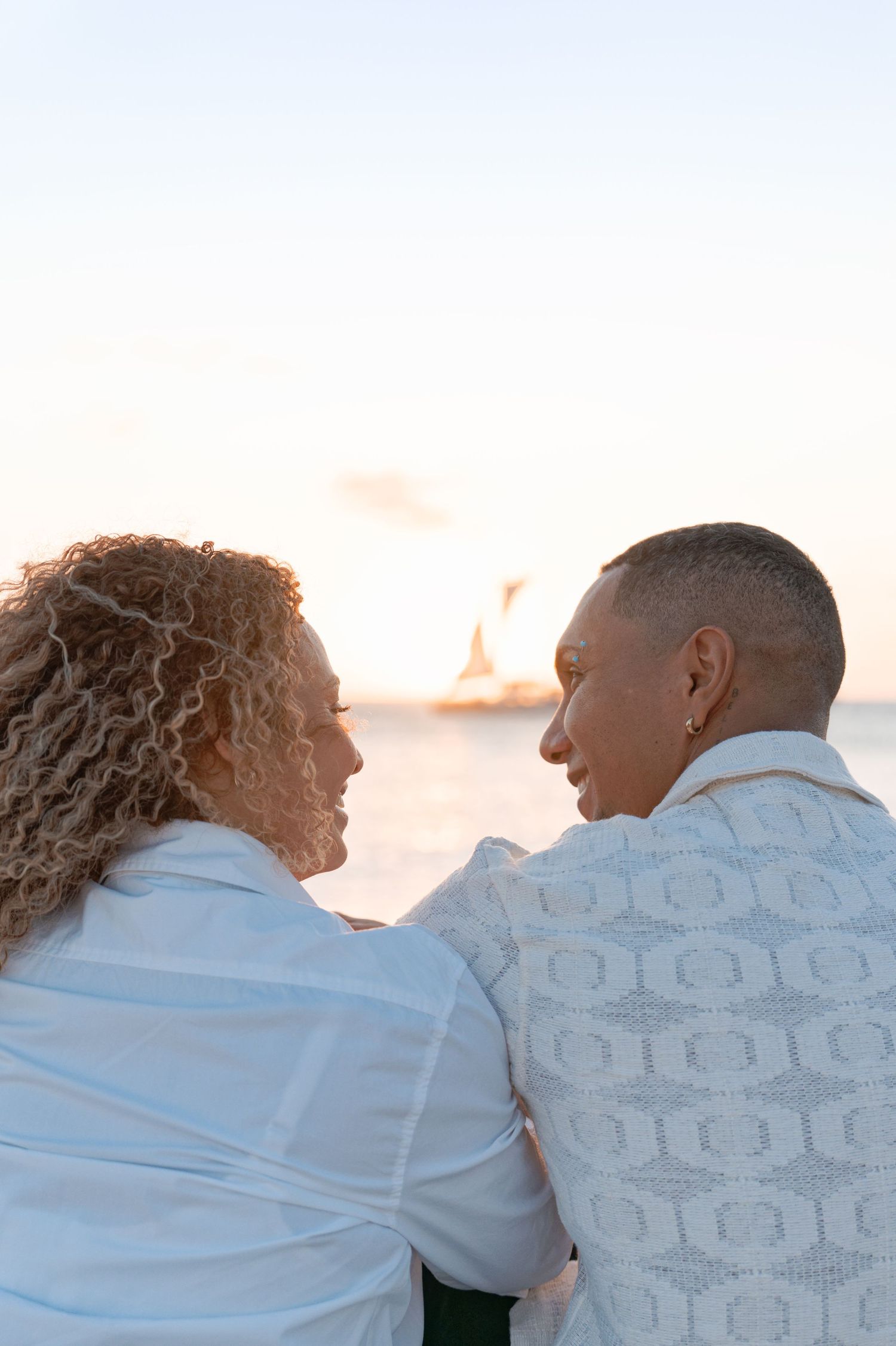 A couple in white shirts sits together watching the sunset over the ocean.