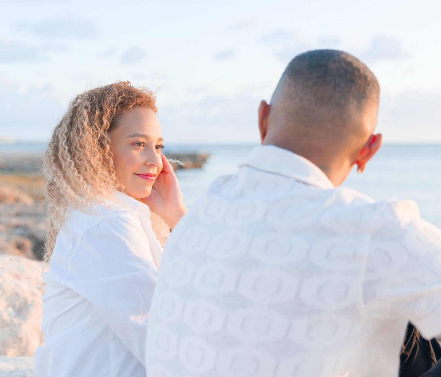 A couple embraces on a beach during sunset, with soft golden light illuminating their silhouettes.