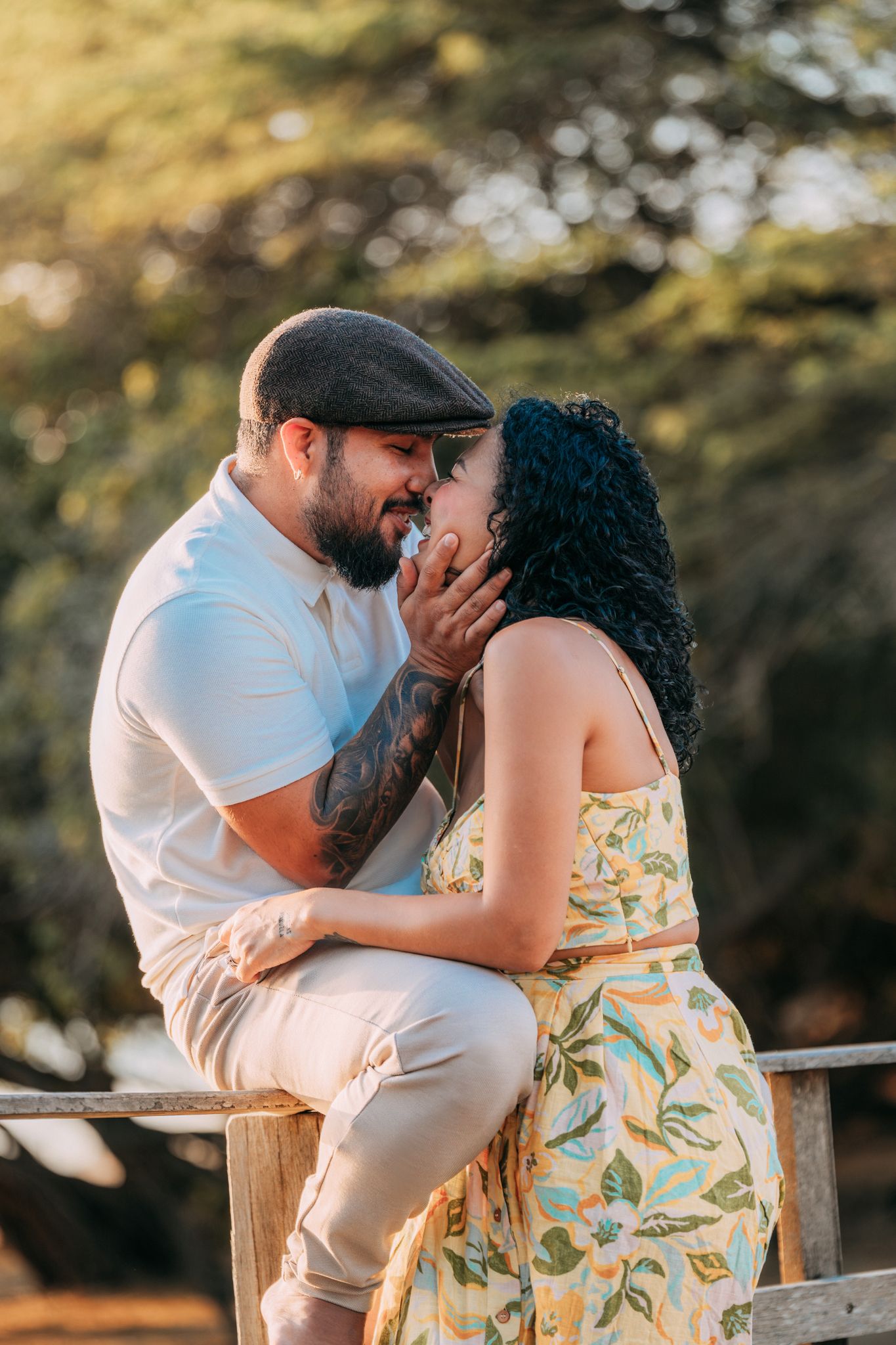 Couple sharing intimate moment while sitting on wooden fence in nature setting.