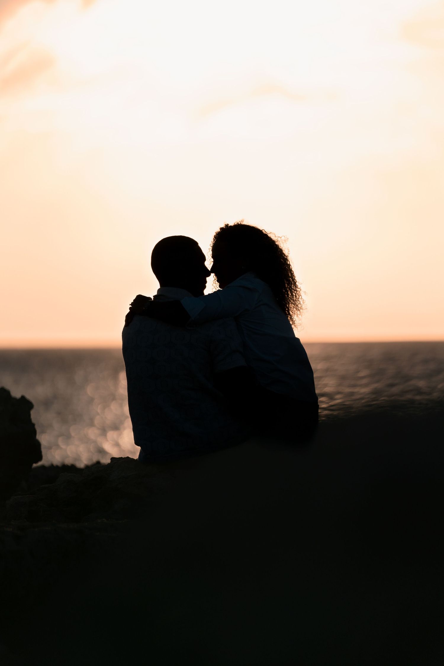 Silhouette of couple against orange sunset sky near ocean.