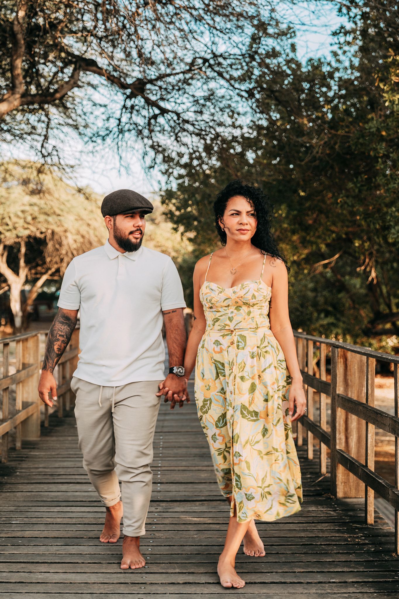Couple walking together on a wooden boardwalk during golden hour, woman wearing floral dress.