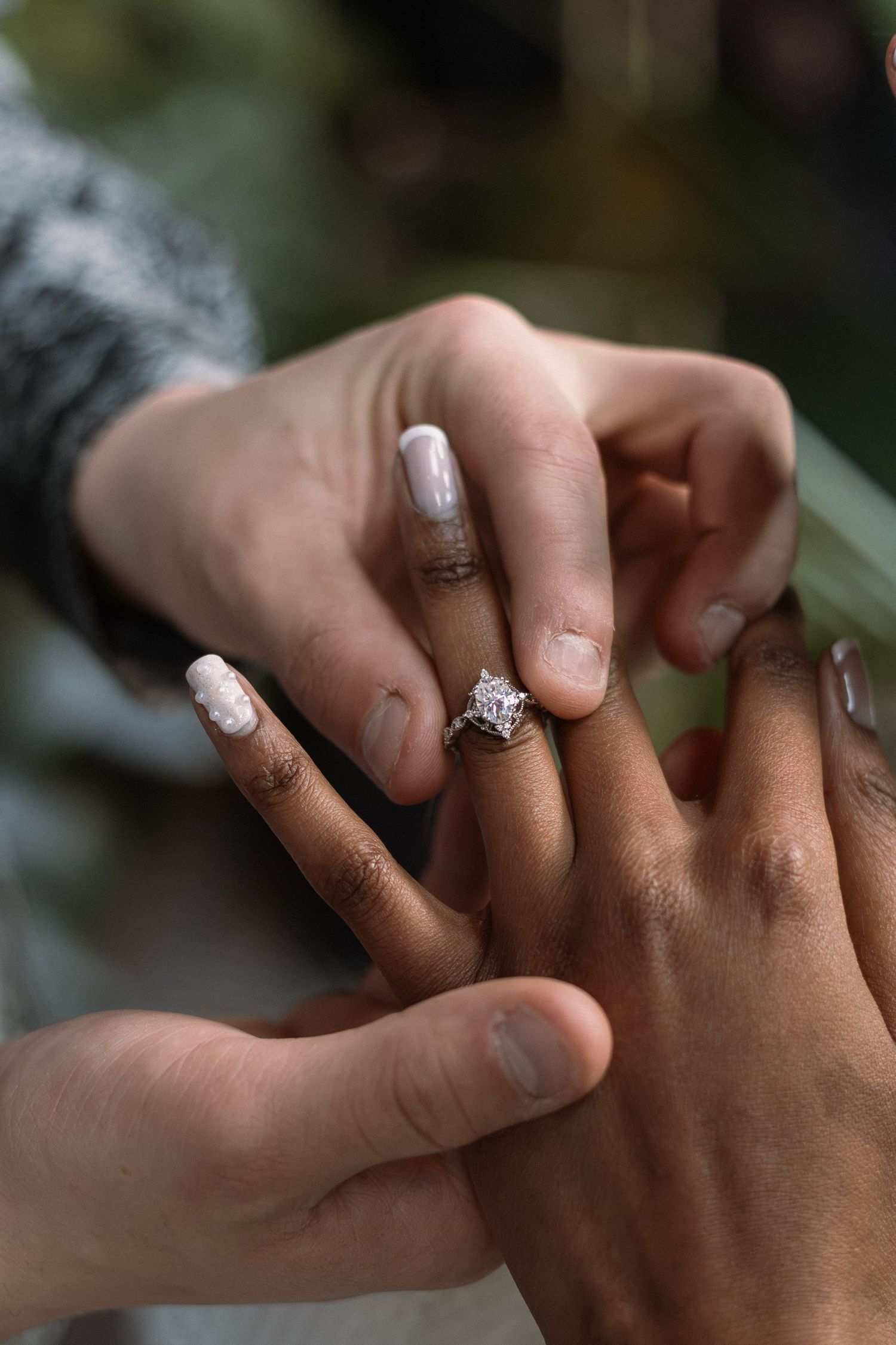 Close-up of an interracial couple sharing an engagement moment, showcasing a stunning diamond ring on the woman's finger.