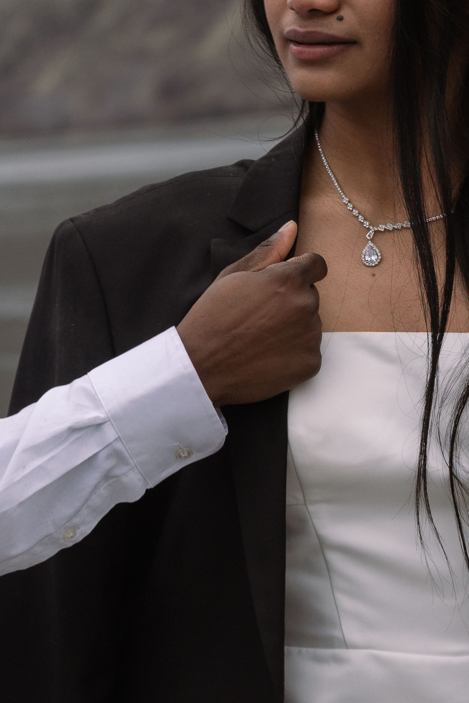 A romantic couple in formal attire share an intimate moment, with focus on jewelry and contrasting black and white clothing.