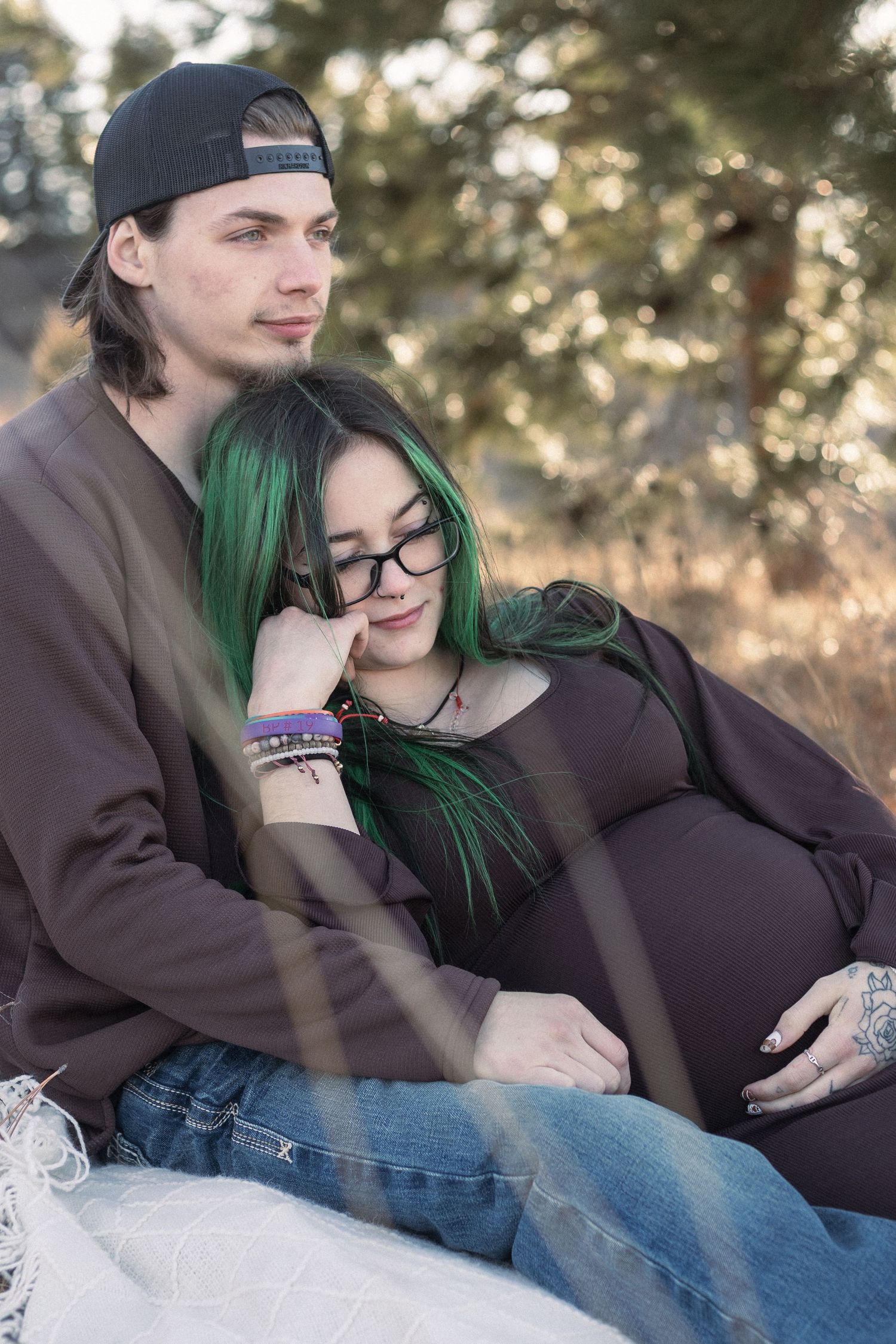Intimate maternity photos of couple relaxing together outdoors in casual winter clothing.