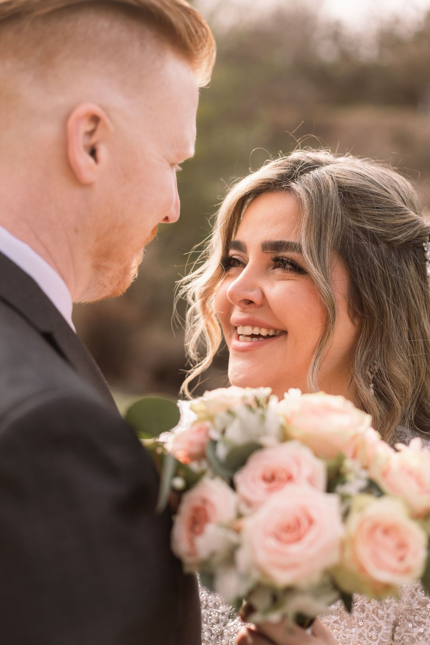 A couple shares an intimate moment on their wedding day with a bouquet of pink roses between them.