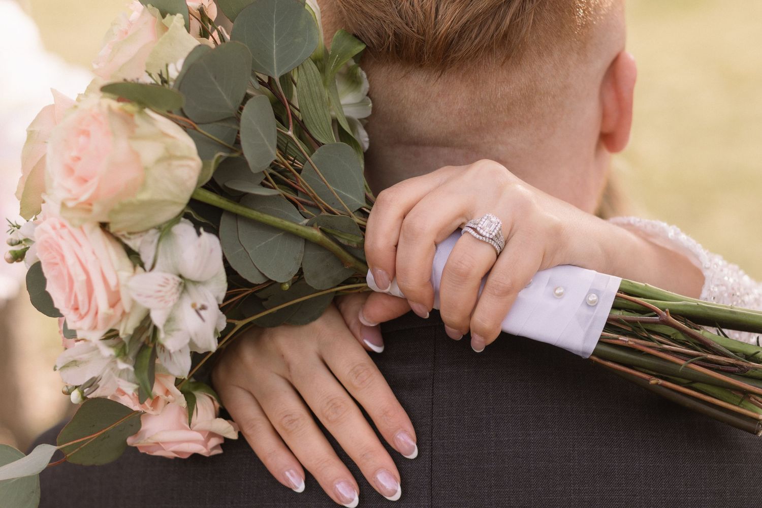 A close-up view of a person's hands holding a bouquet of pink roses and greenery.