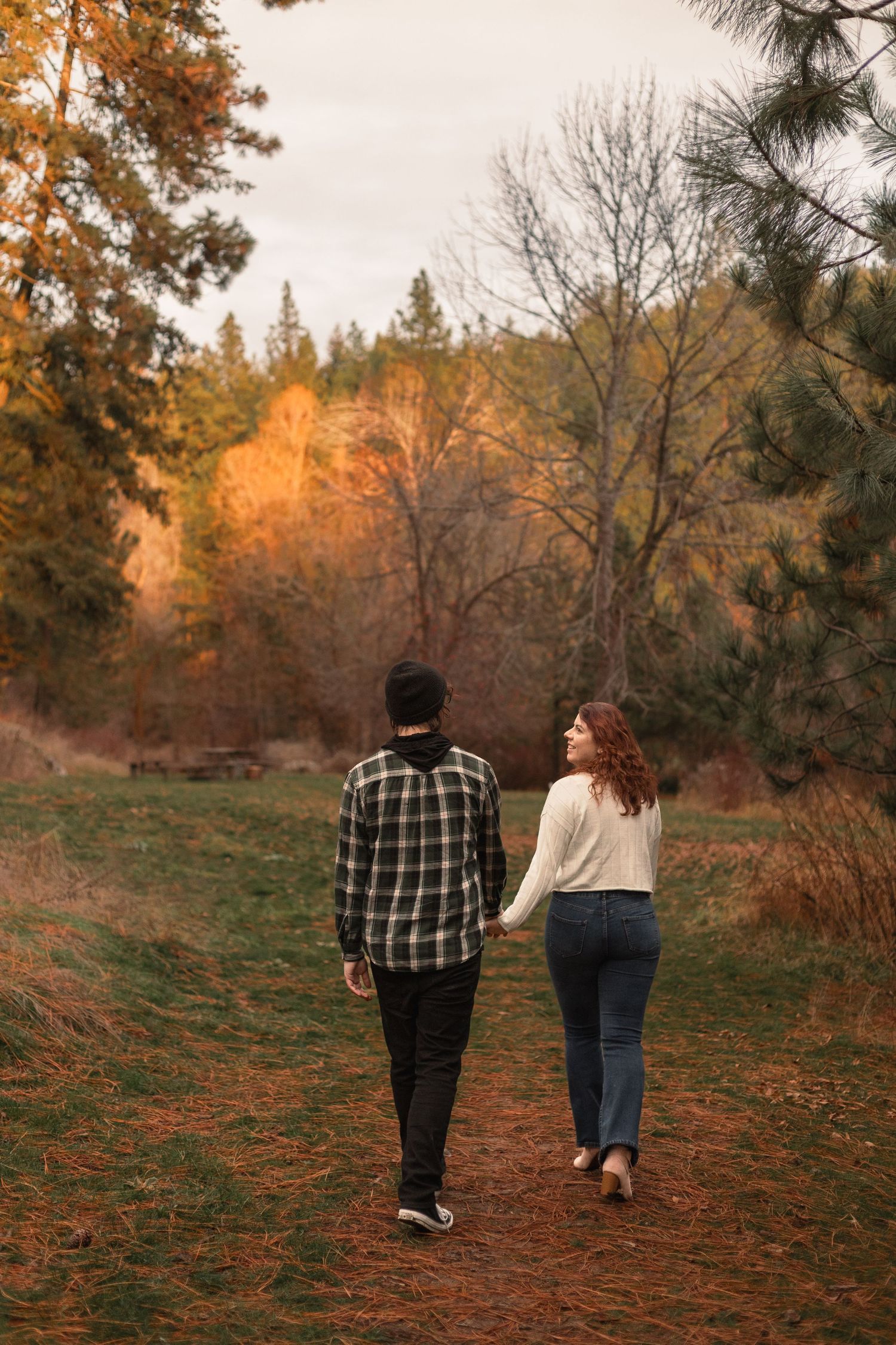 Couple walking hand in hand through a forest path during golden autumn sunset.