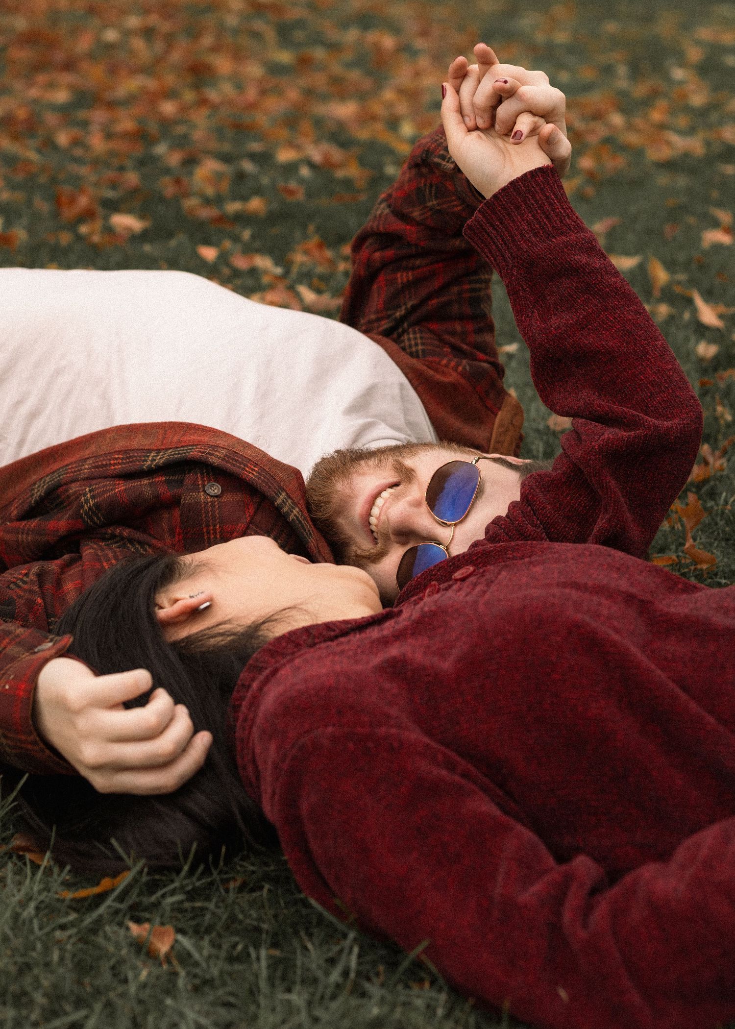 Person in burgundy sweater relaxing on fallen autumn leaves during outdoor photoshoot.