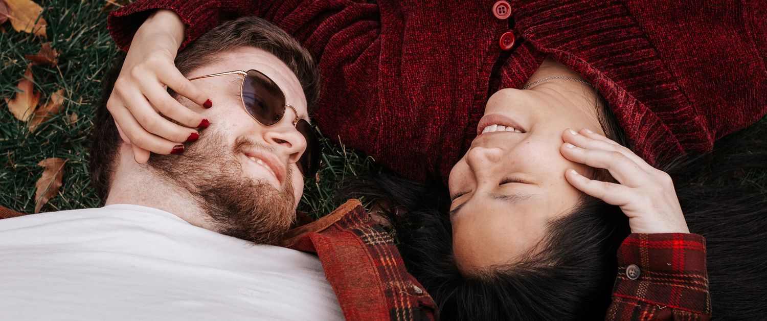 Two people lying on autumn leaves making silly faces outdoors.