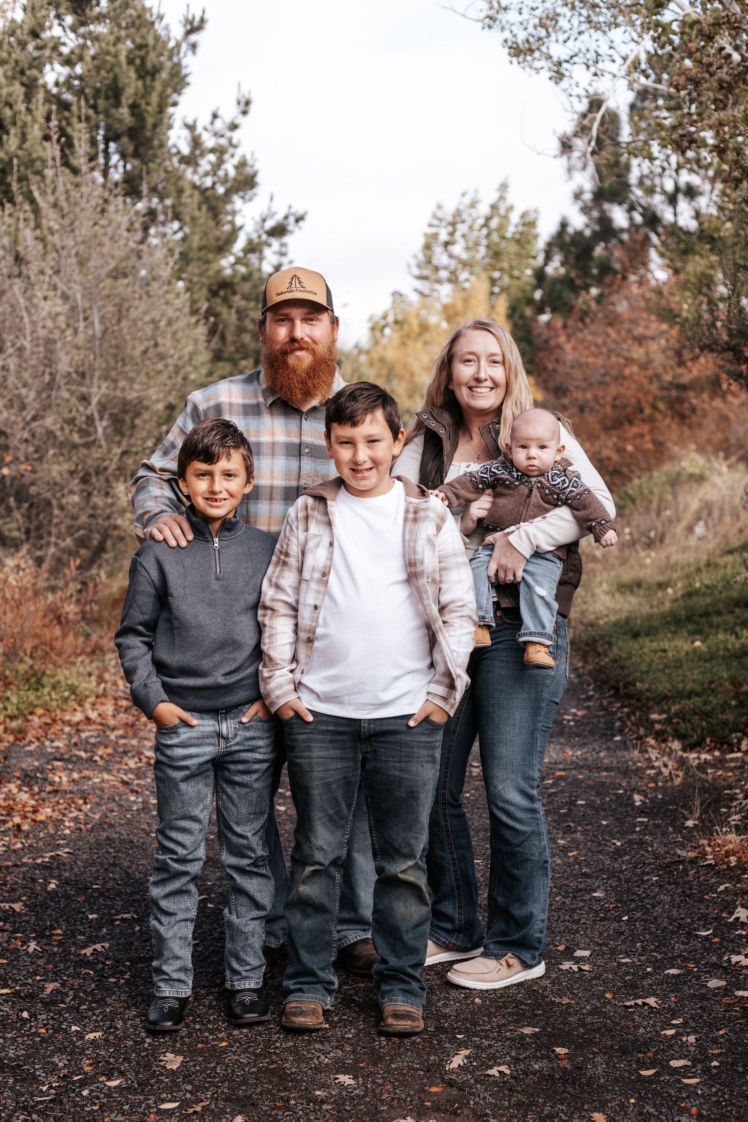 A family poses together on a dirt path surrounded by autumn trees and foliage.
