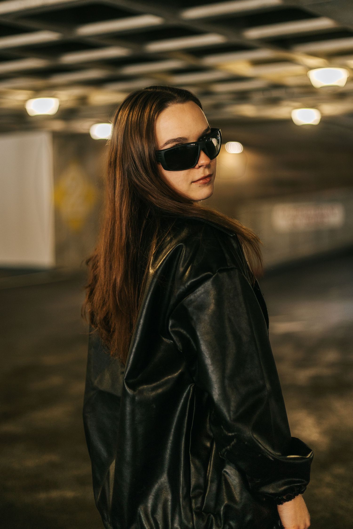 Stylish portrait with sunglasses and leather jacket in underground parking structure.