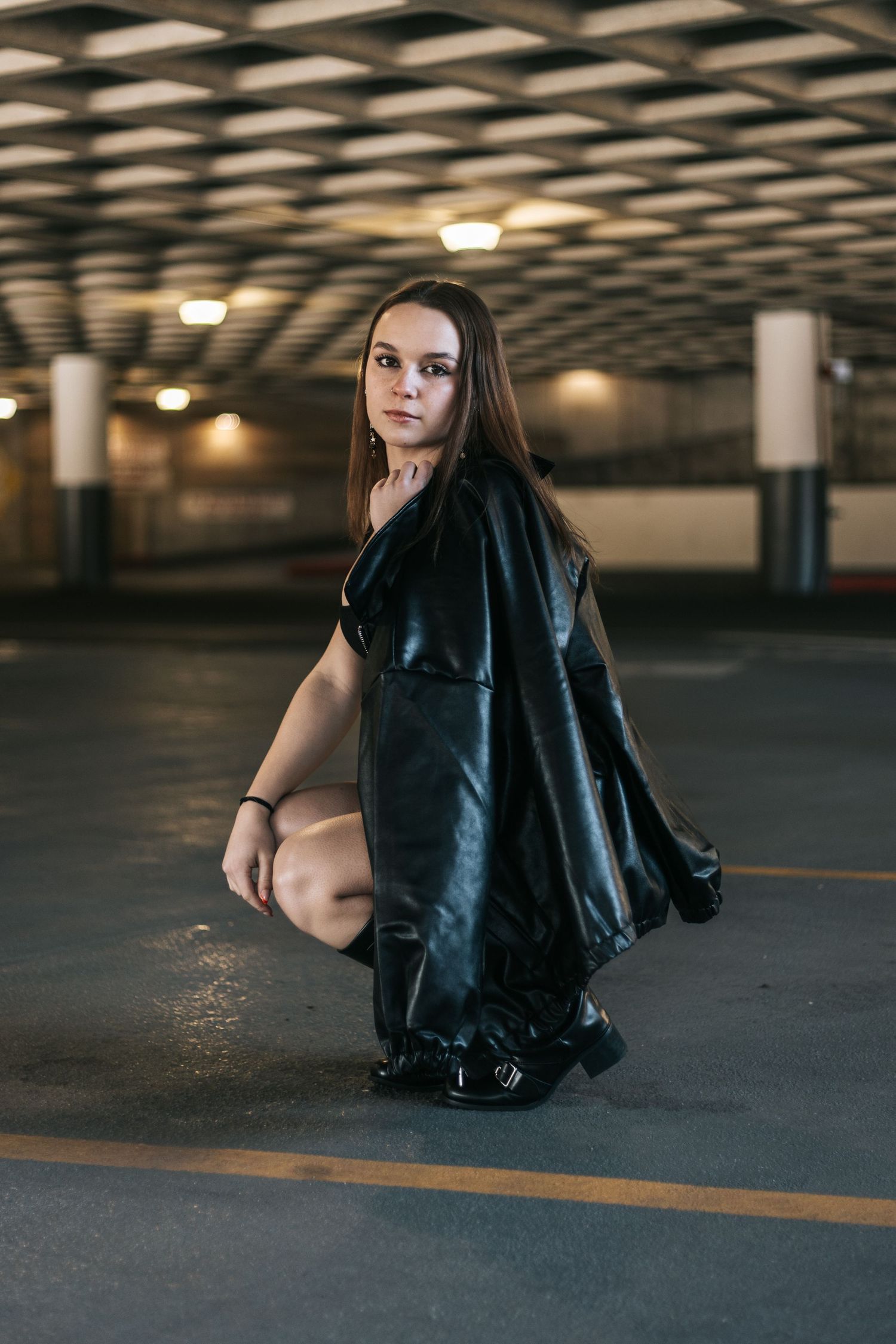 Moody fashion portrait of someone posing in black outfit in a dimly lit parking garage.