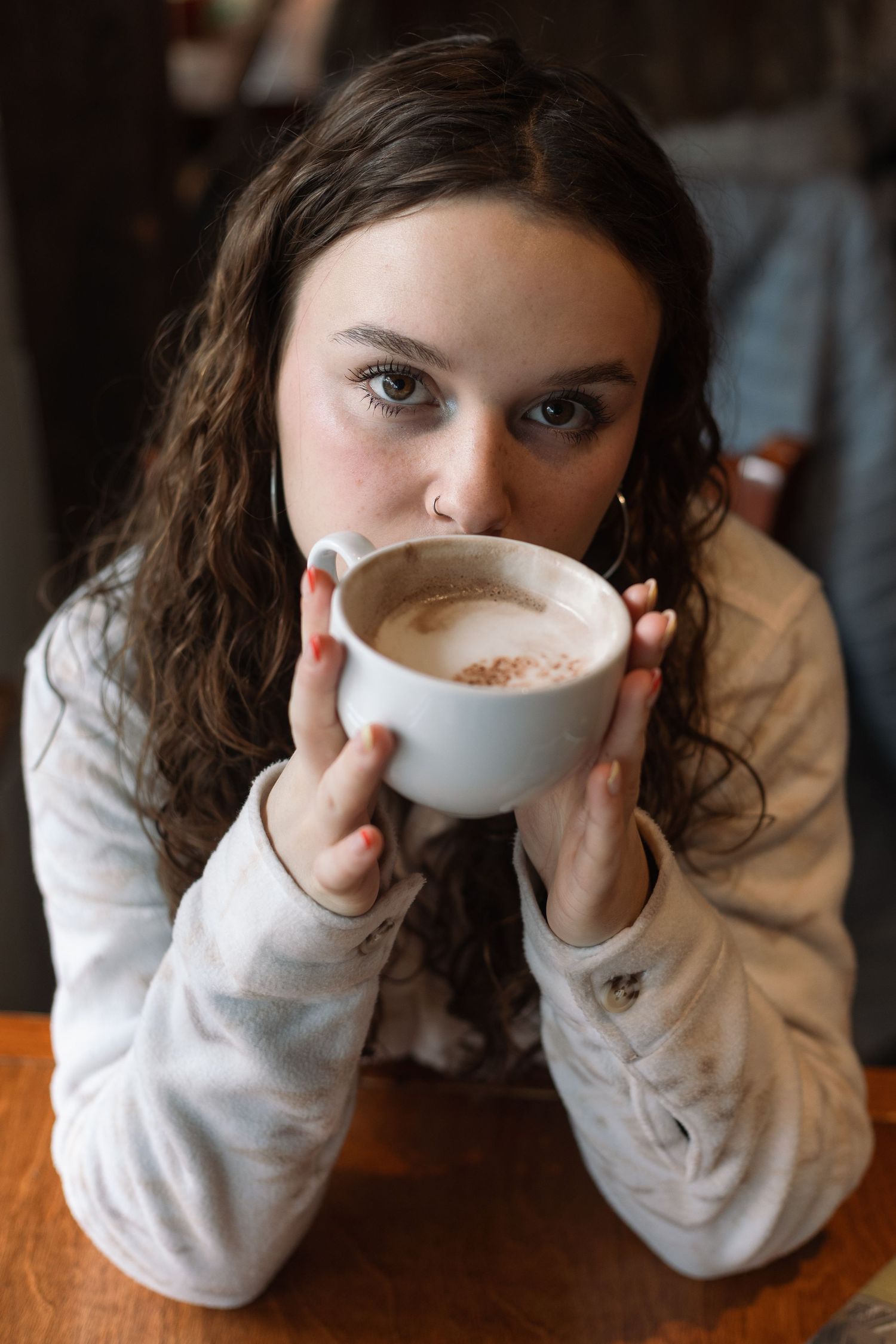 Intimate portrait of someone sipping from white coffee cup in cafe setting.