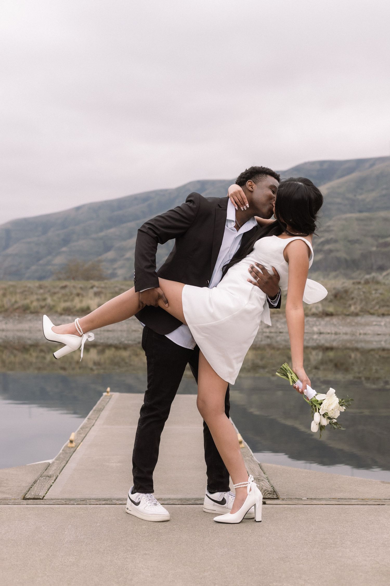 A romantic dip pose during a lakeside wedding photoshoot with mountain scenery.